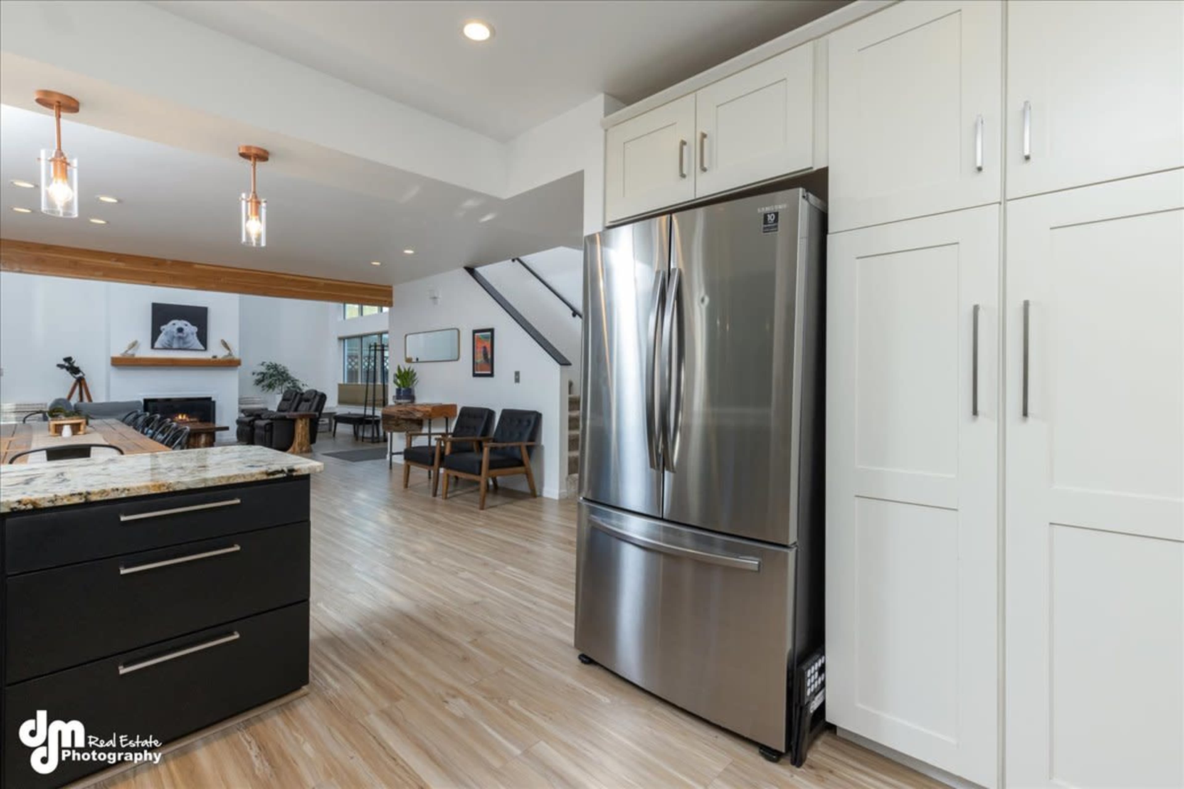 A modern kitchen with stainless steel appliances and an open layout leading to a living area furnished with chairs and wooden accents.