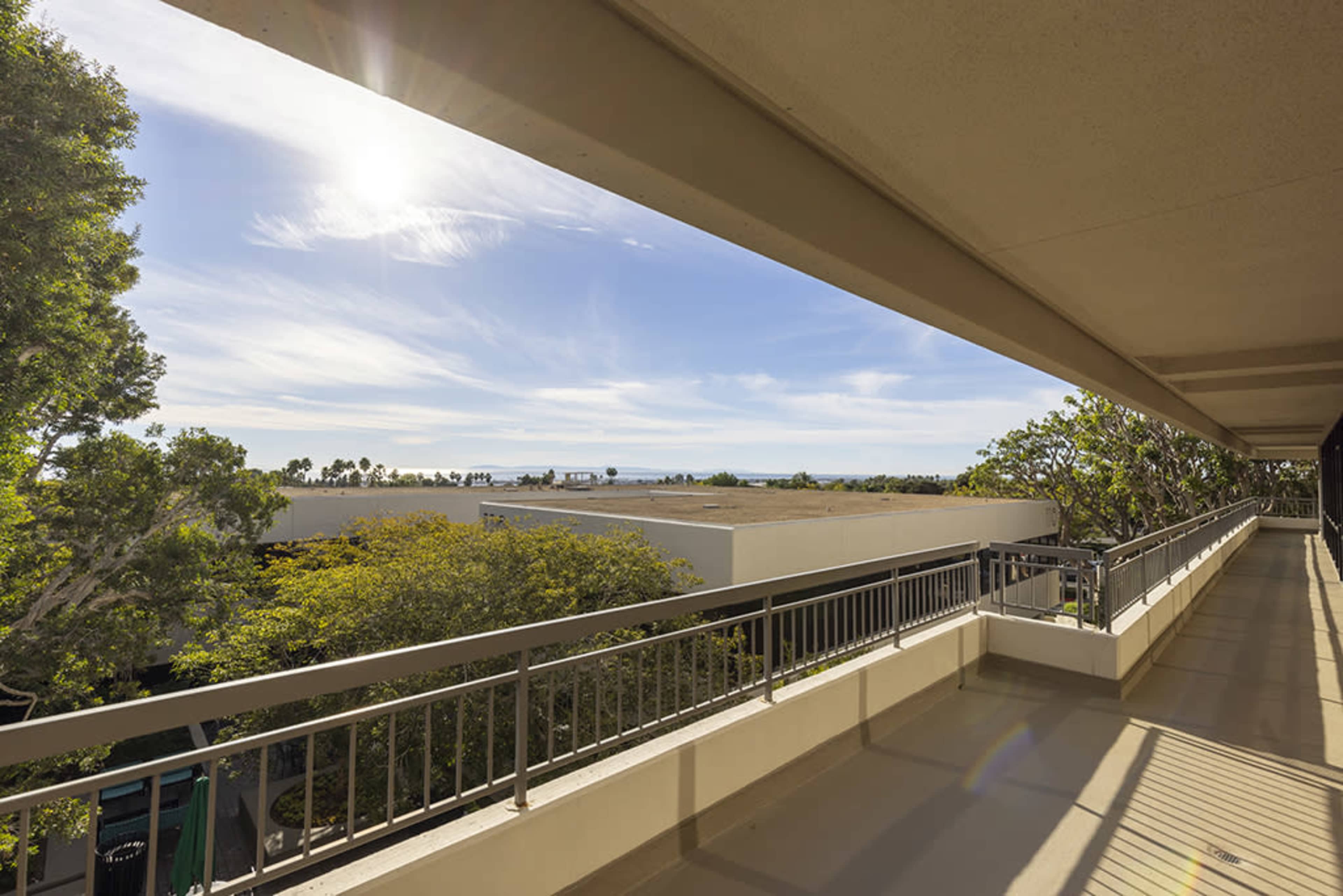 A balcony overlooking a landscape with trees and a view of the ocean in the distance under a clear sky.