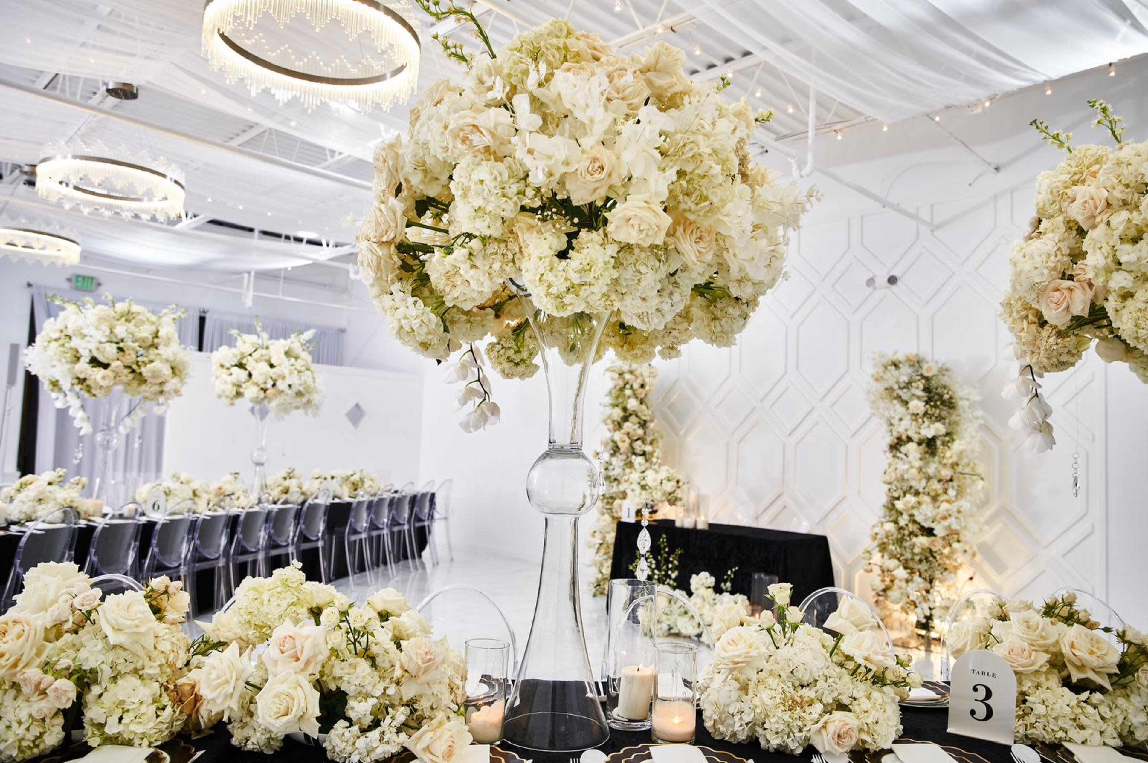 A banquet hall is elegantly arranged with tall floral centerpieces and tables set for an event.