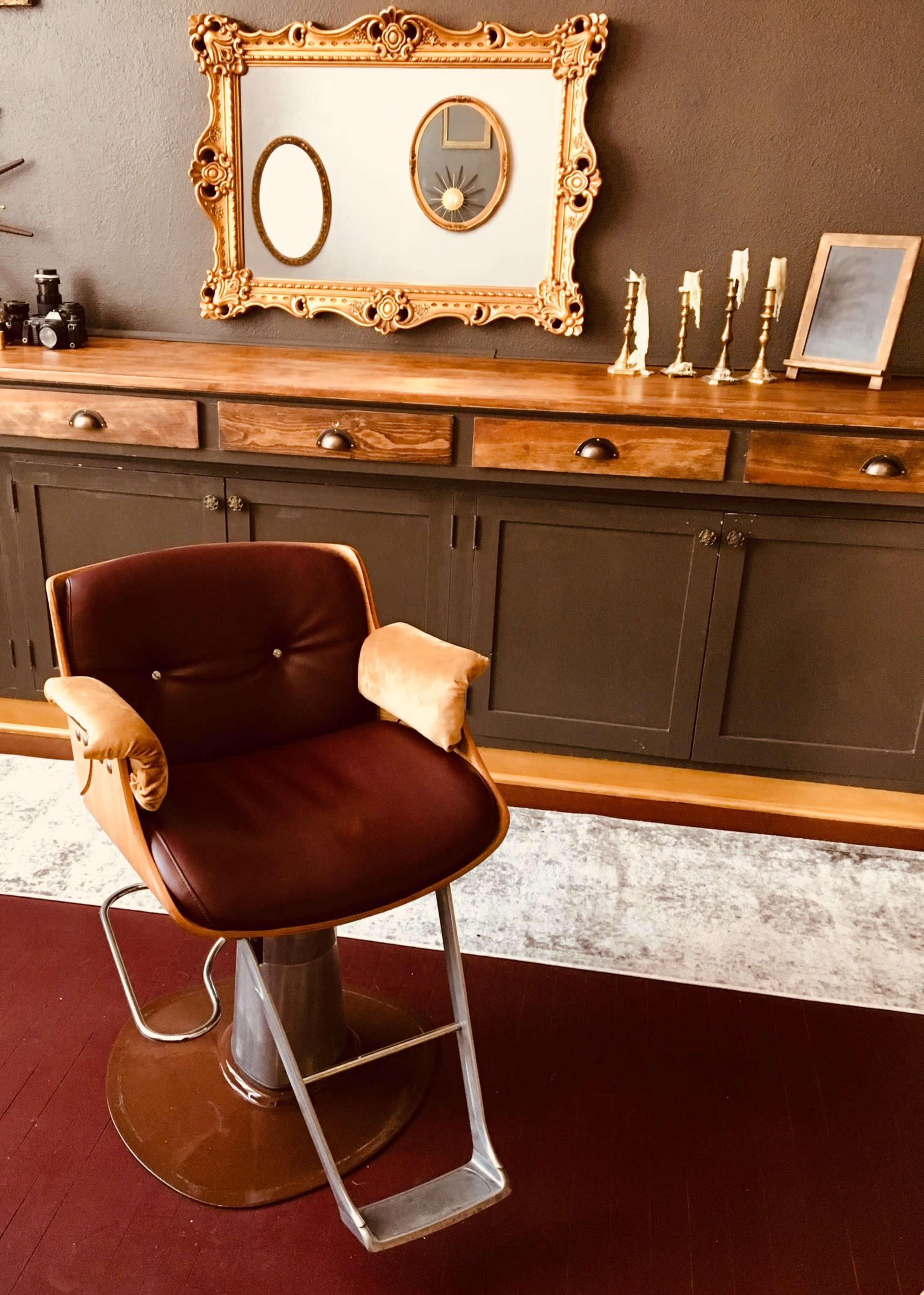 A vintage barber chair positioned in front of a wooden sideboard with decorative mirrors and candles.