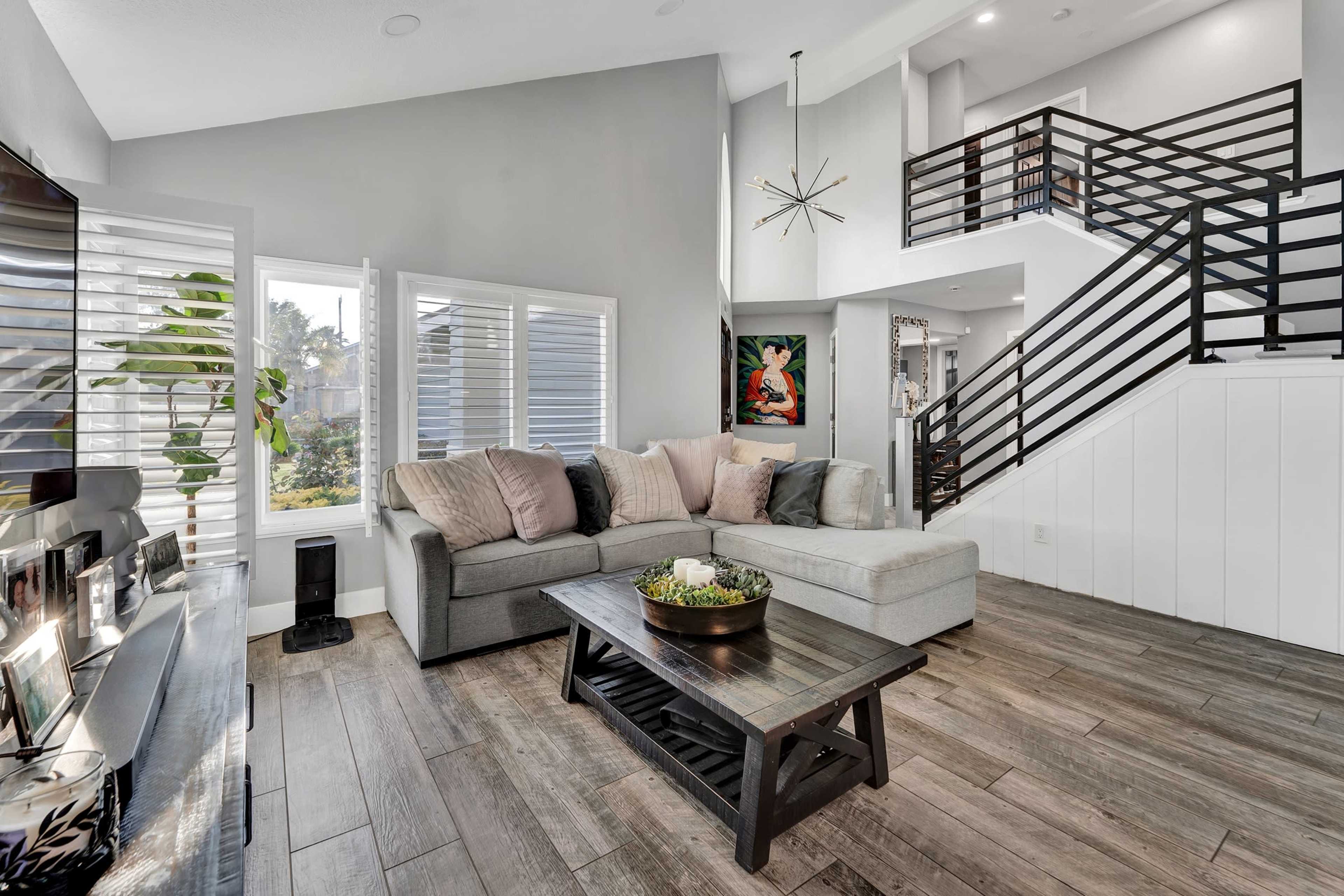 A modern living room with a gray sectional sofa, a coffee table, and a staircase leading to an upper level.
