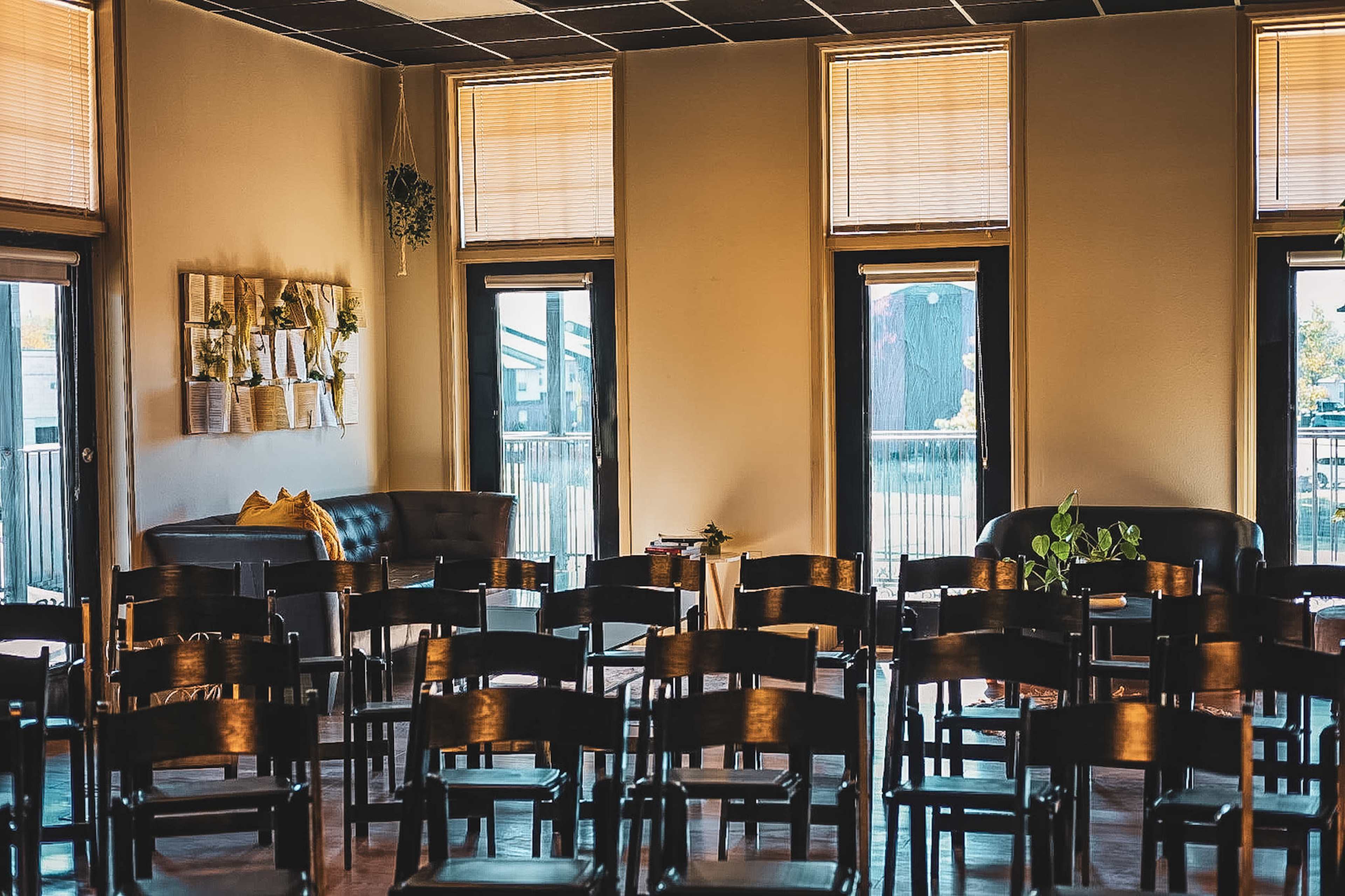 The image shows a room with several wooden chairs arranged in rows facing large windows, revealing outdoor views.