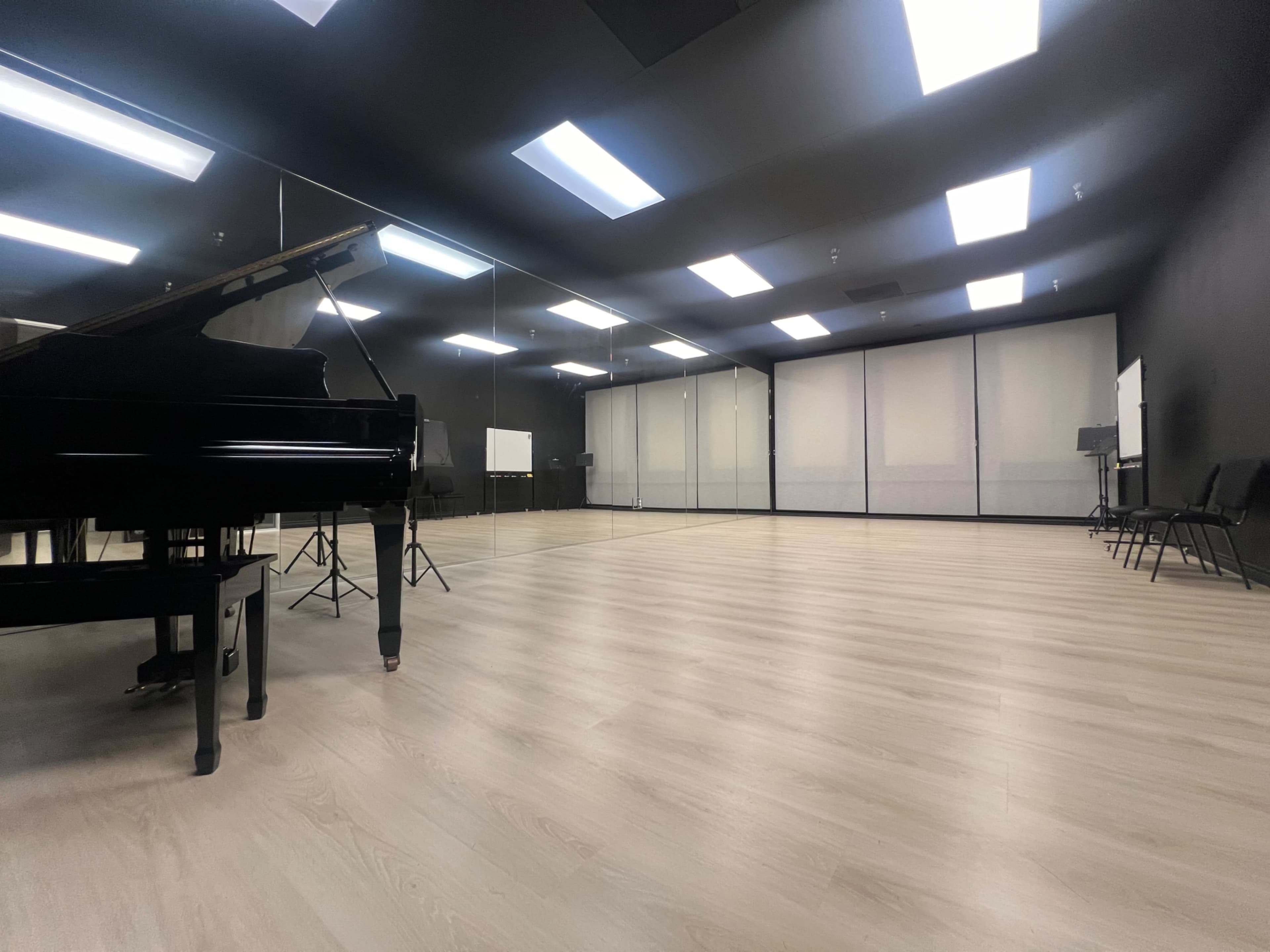 The image shows a spacious music rehearsal room with a grand piano on the left and mirrors lining the back wall.