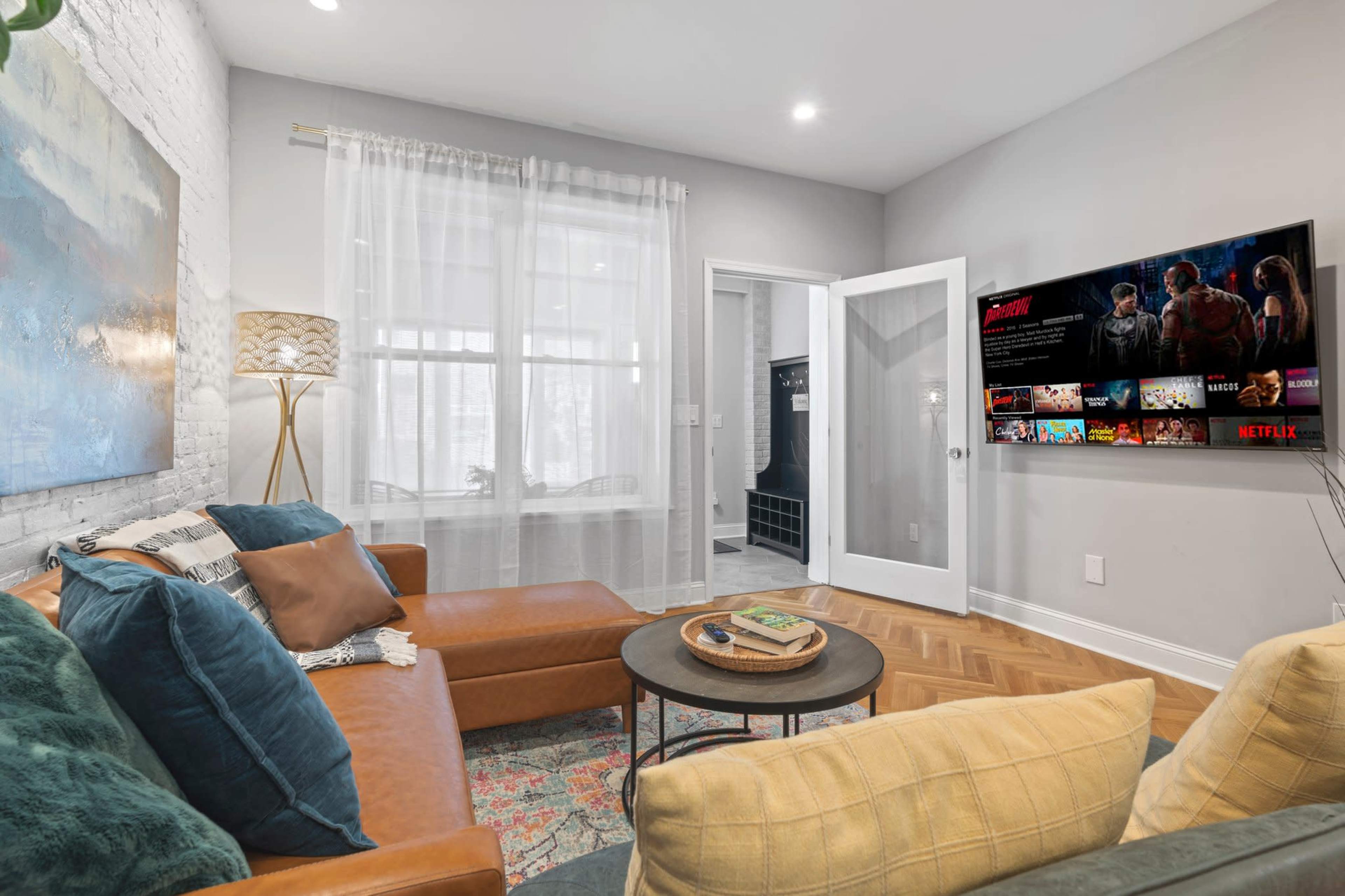 A cozy living room features a sectional sofa, a round coffee table, and a wall-mounted TV displaying a streaming service.