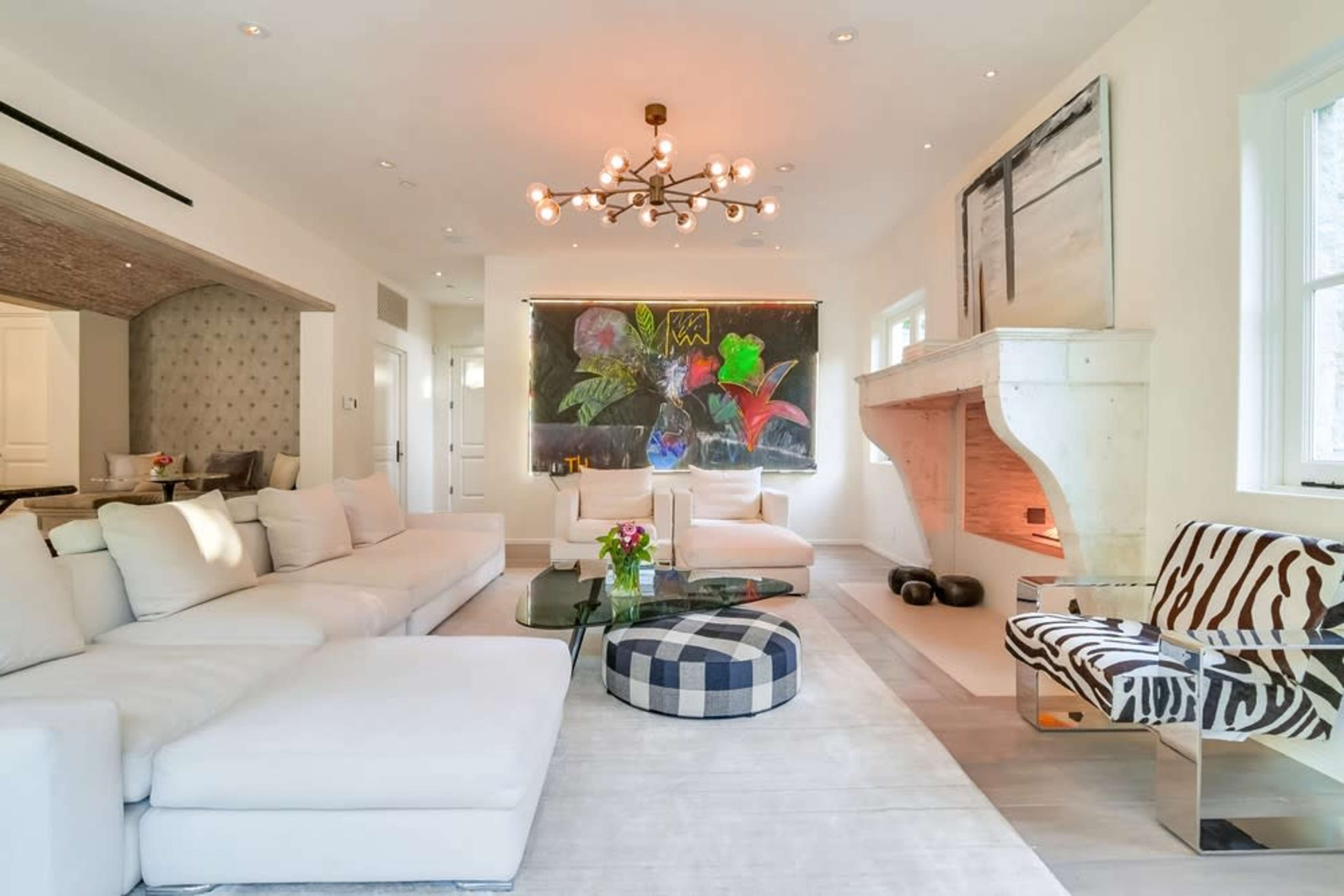 A modern living room features a large white sectional sofa, a decorative coffee table, and a striking artwork above a stone fireplace.