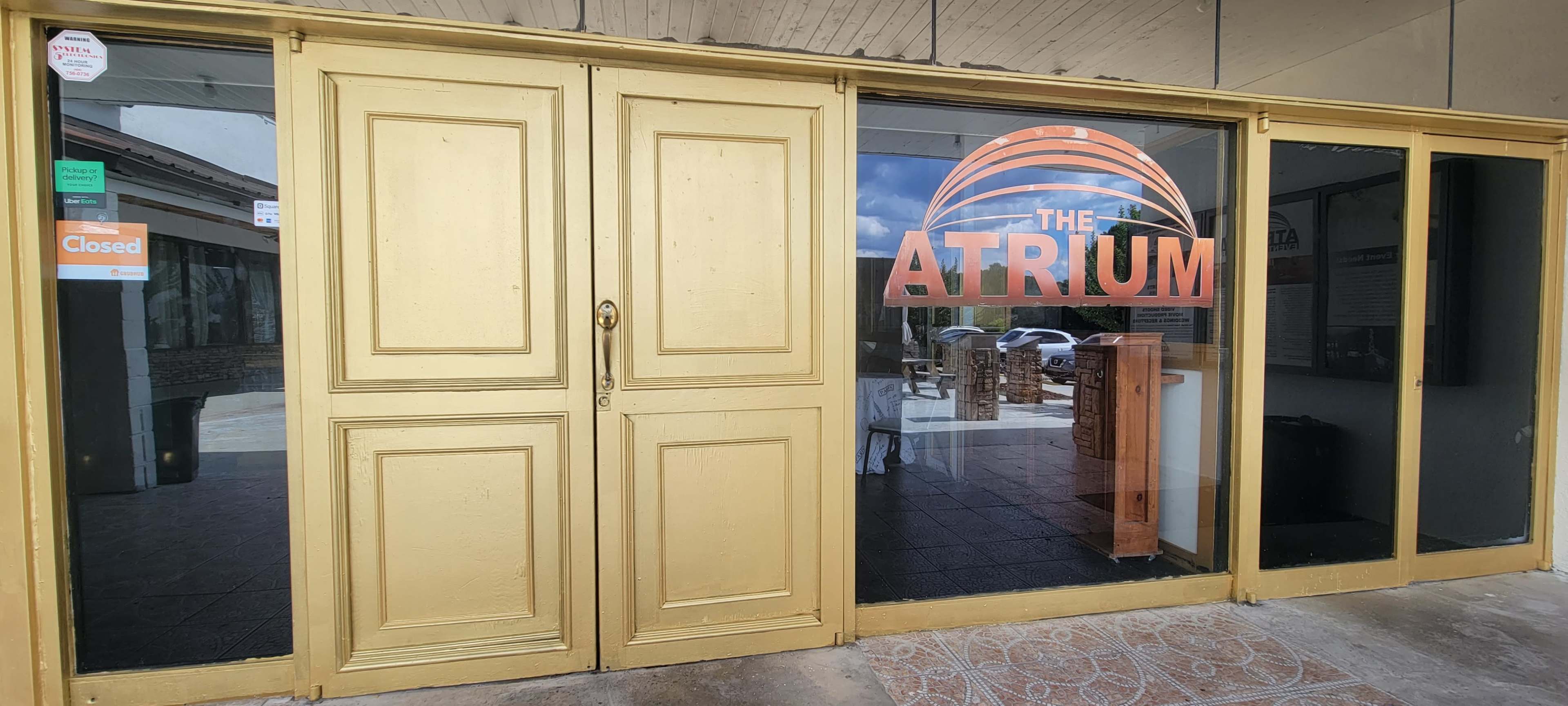 The entrance of a building named "The Atrium" features large golden double doors and a glass window displaying the name prominently, with a sign indicating it is closed.