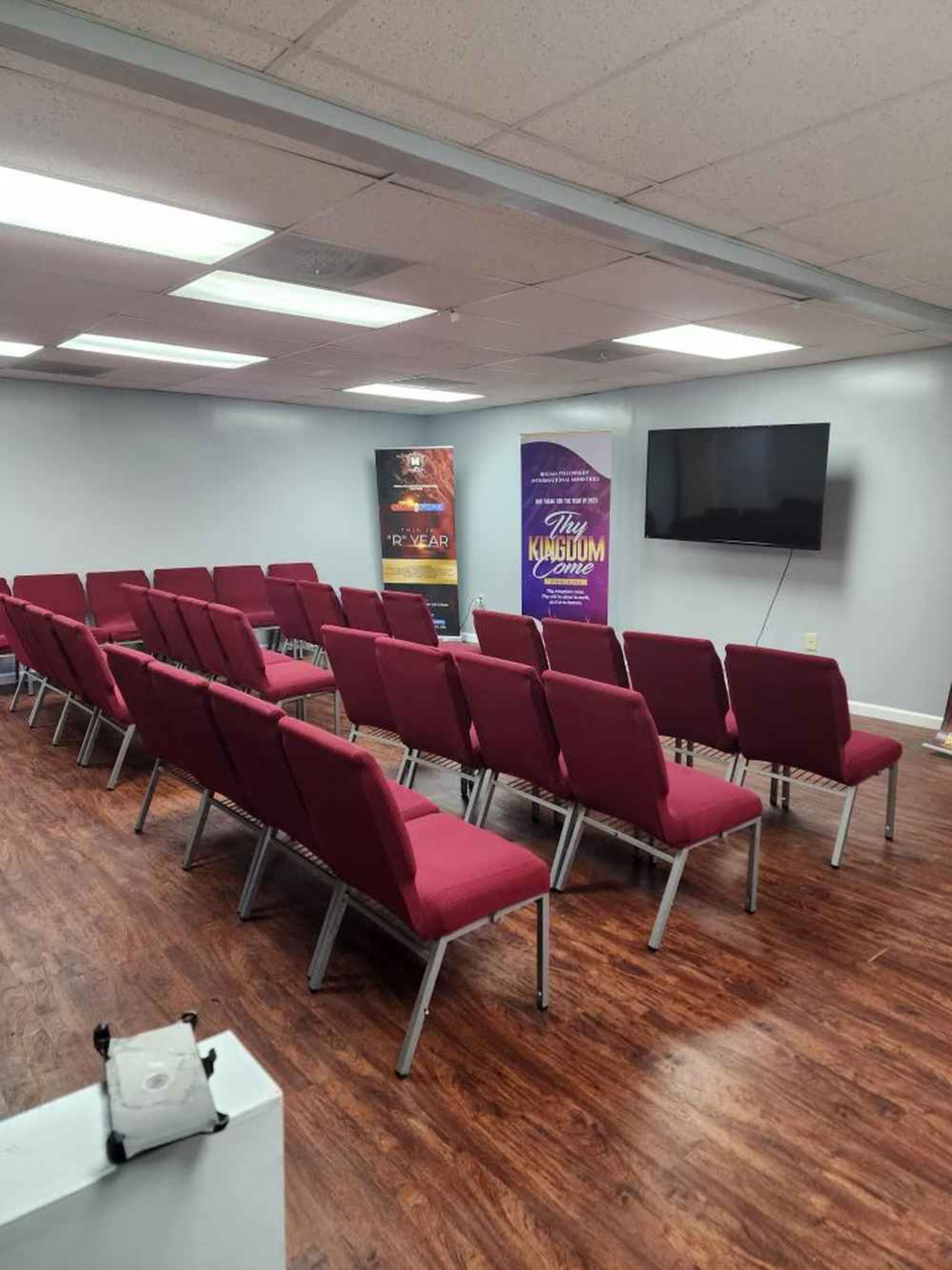 A room set up with red chairs arranged in rows facing a television screen and decorative banners on the walls.