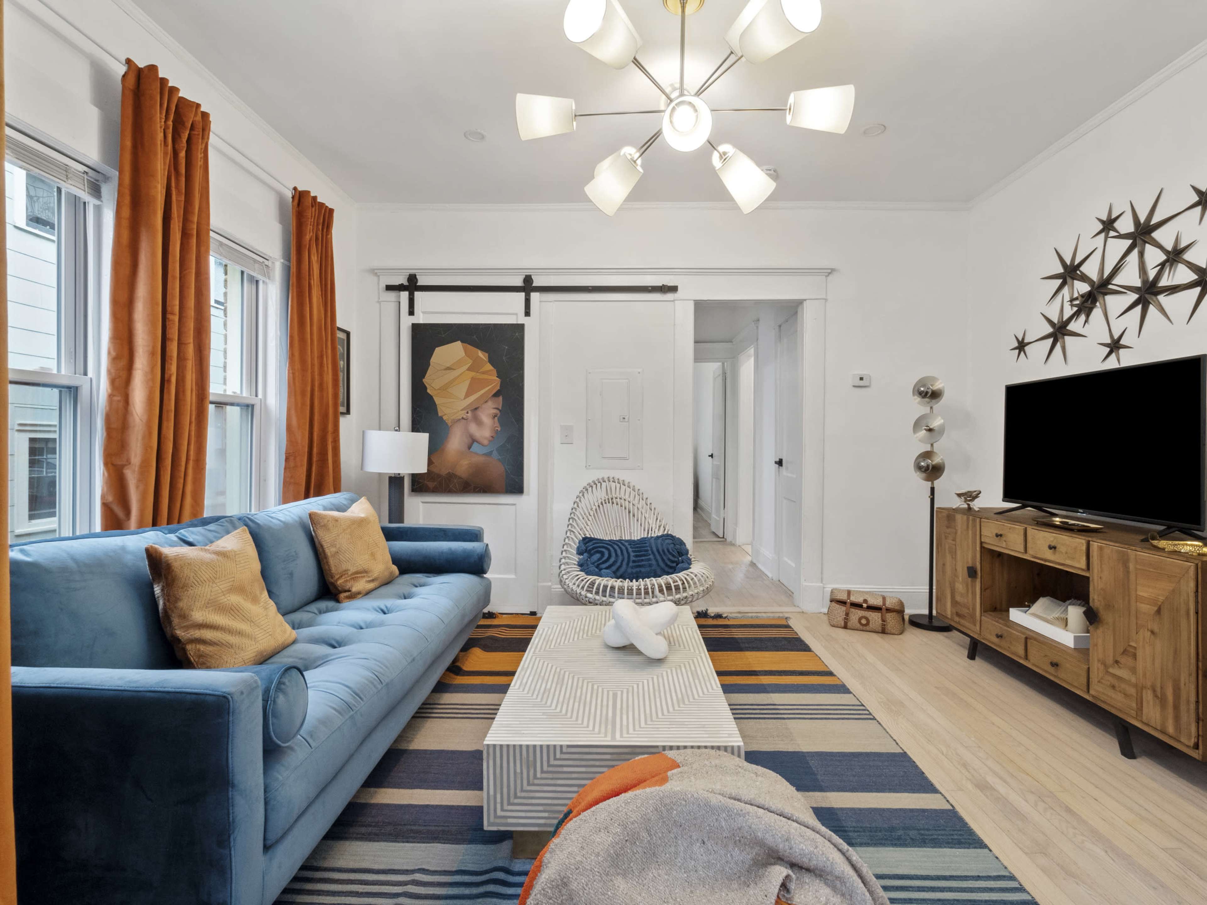 The living room features a blue sofa, a round chair, a striped rug, a wooden TV stand, and a striking wall art piece.
