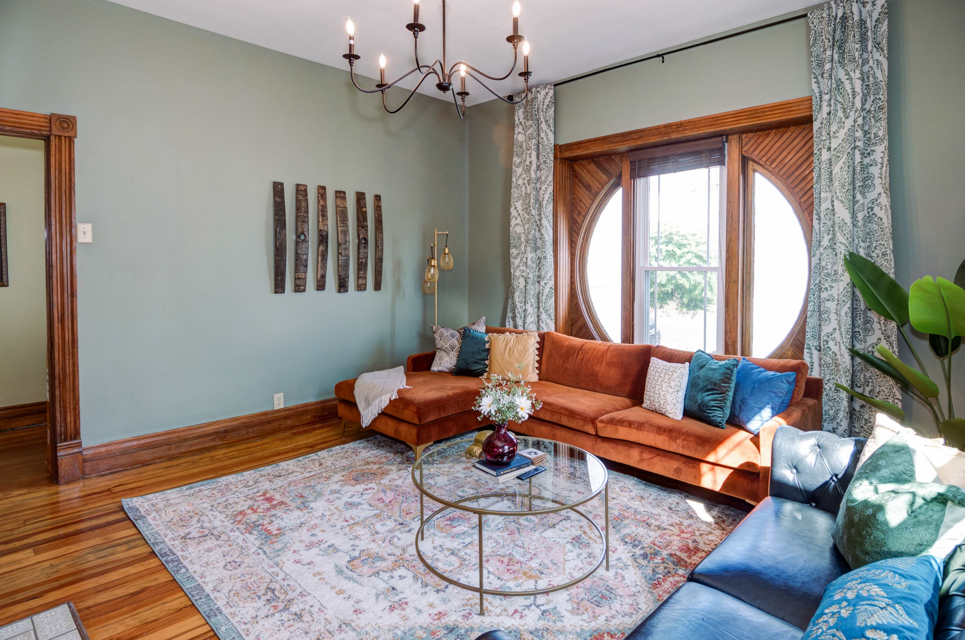 A living room with a circular window, a brown sectional sofa, and a round coffee table on a decorative rug.