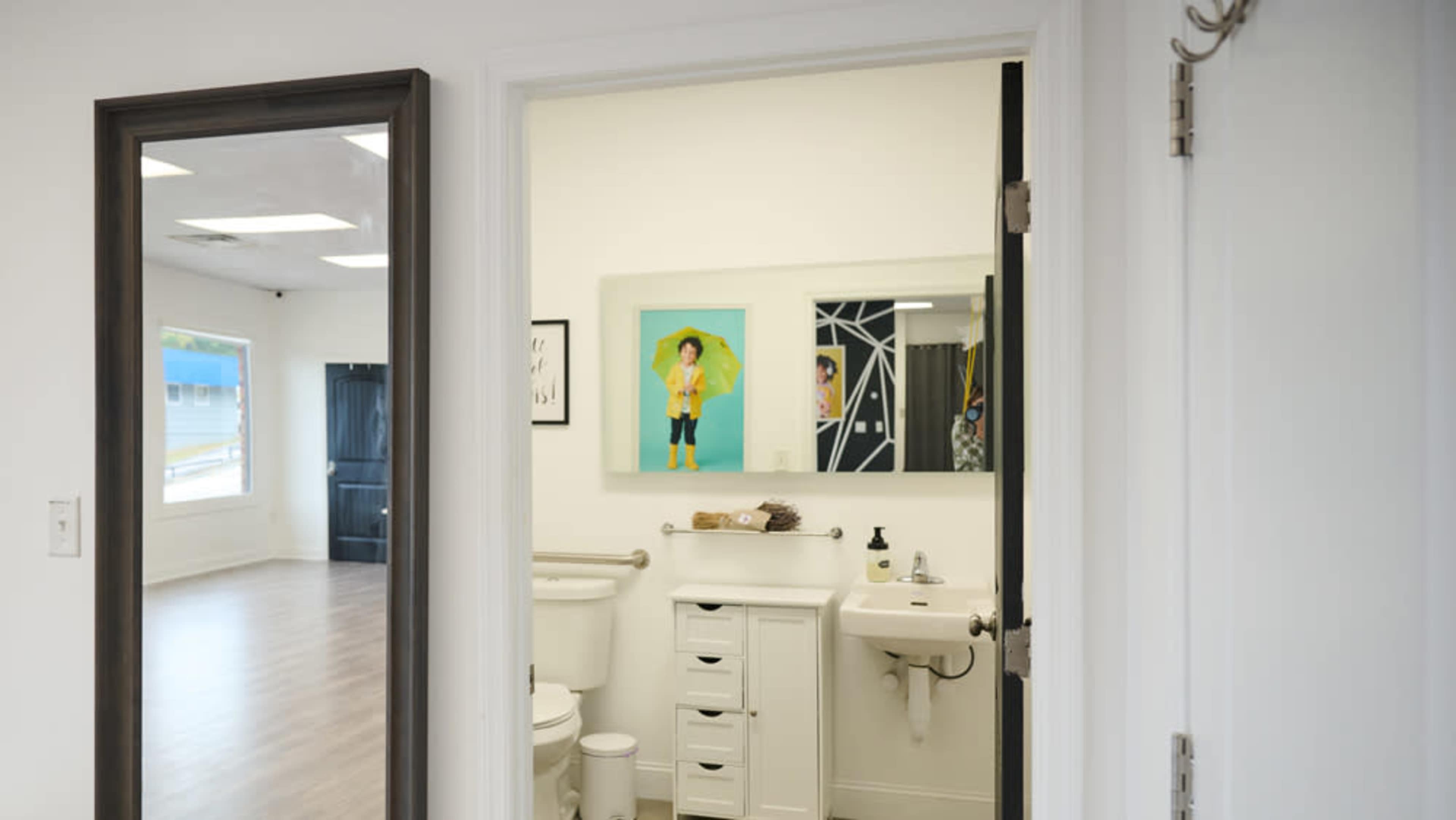 A bathroom is visible through an open door, featuring a white toilet, sink, and a decorative mirror, while a brightly lit room is seen through another open doorway.