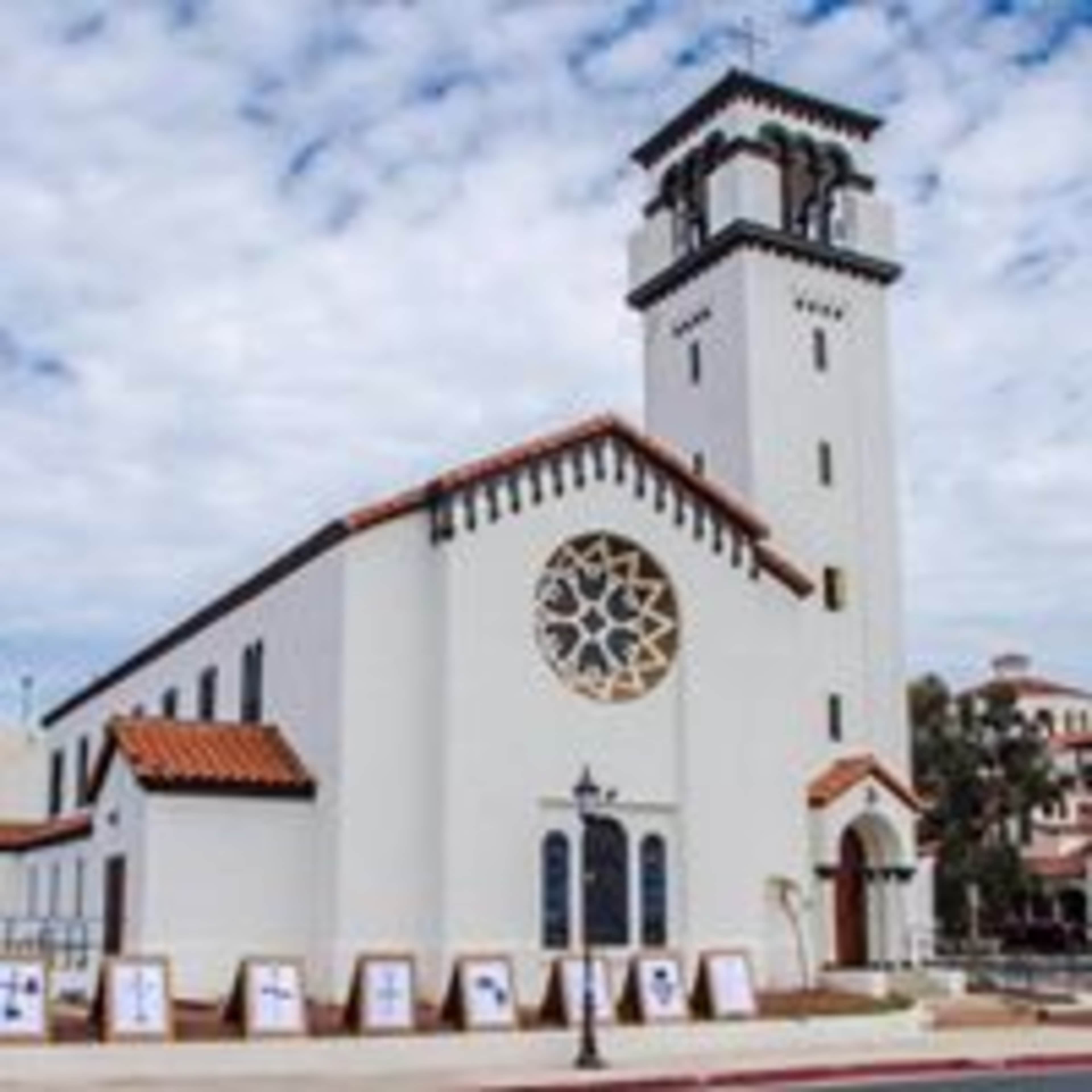 A white church building with a tall bell tower and decorative rose window, located in a suburban area.