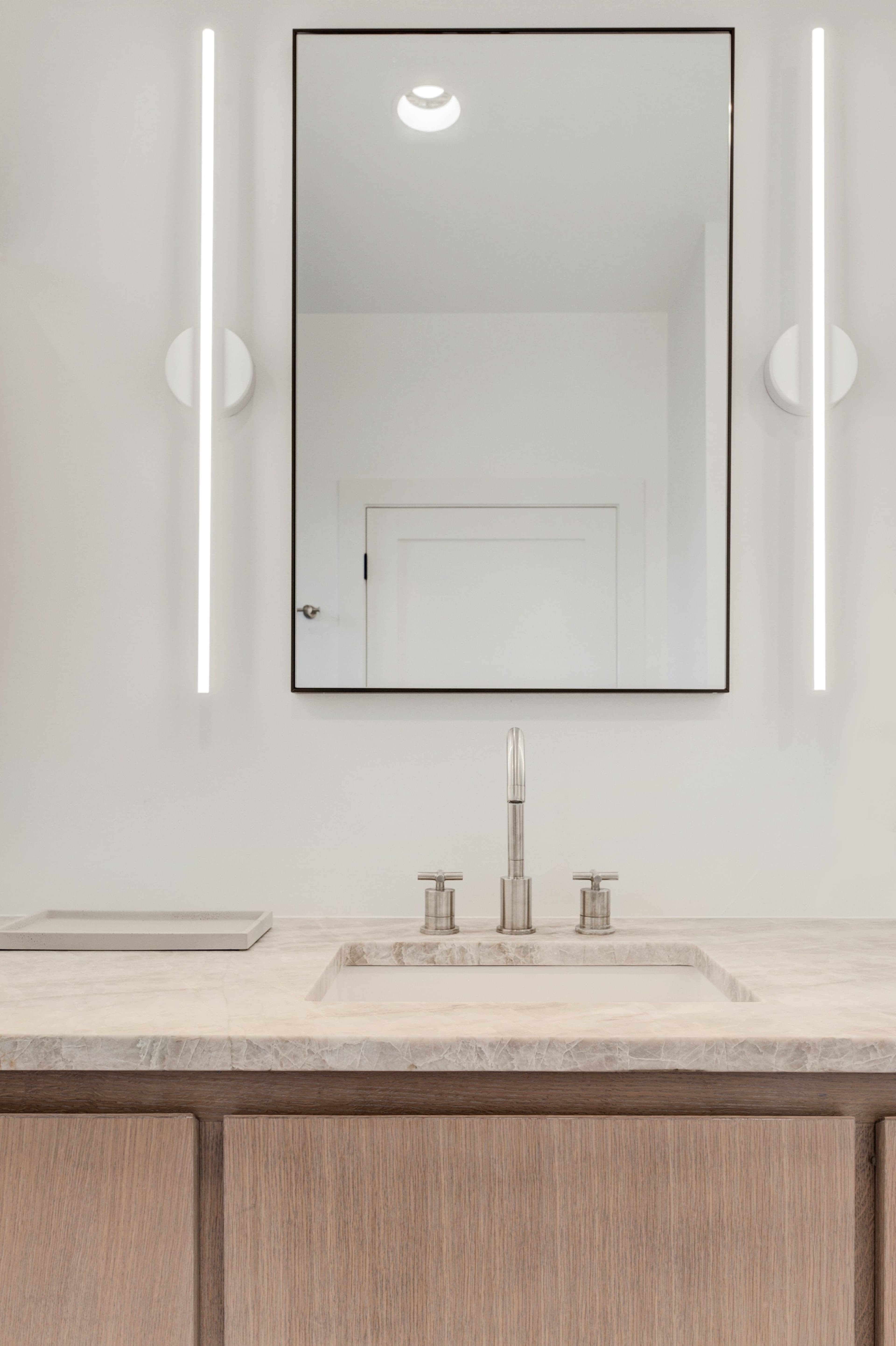A bathroom vanity with a sink, a faucet, and a rectangular mirror illuminated by two vertical light fixtures.