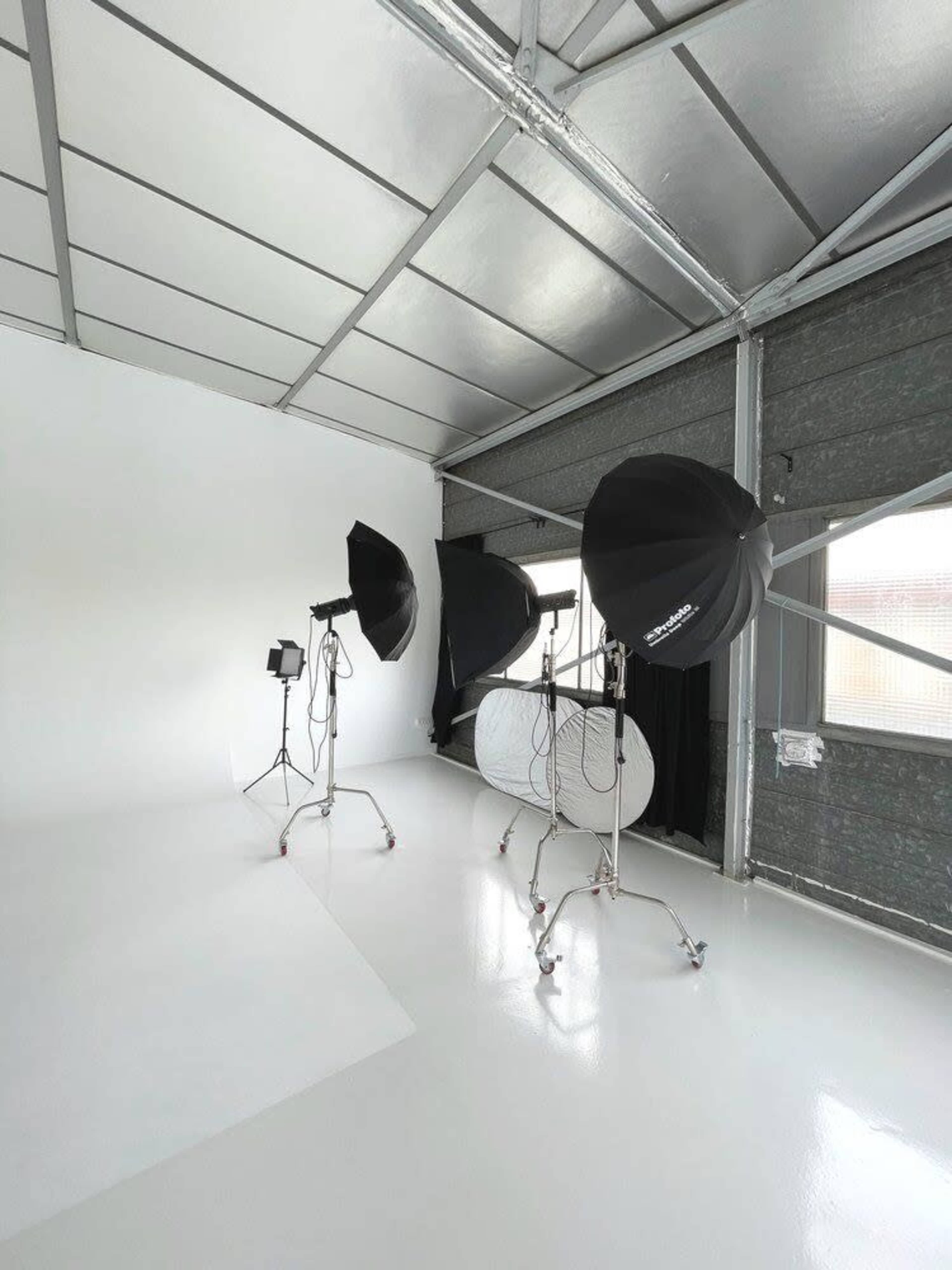 The image shows a photography studio with three softbox lights and a large reflector set up on a white floor and backdrop.
