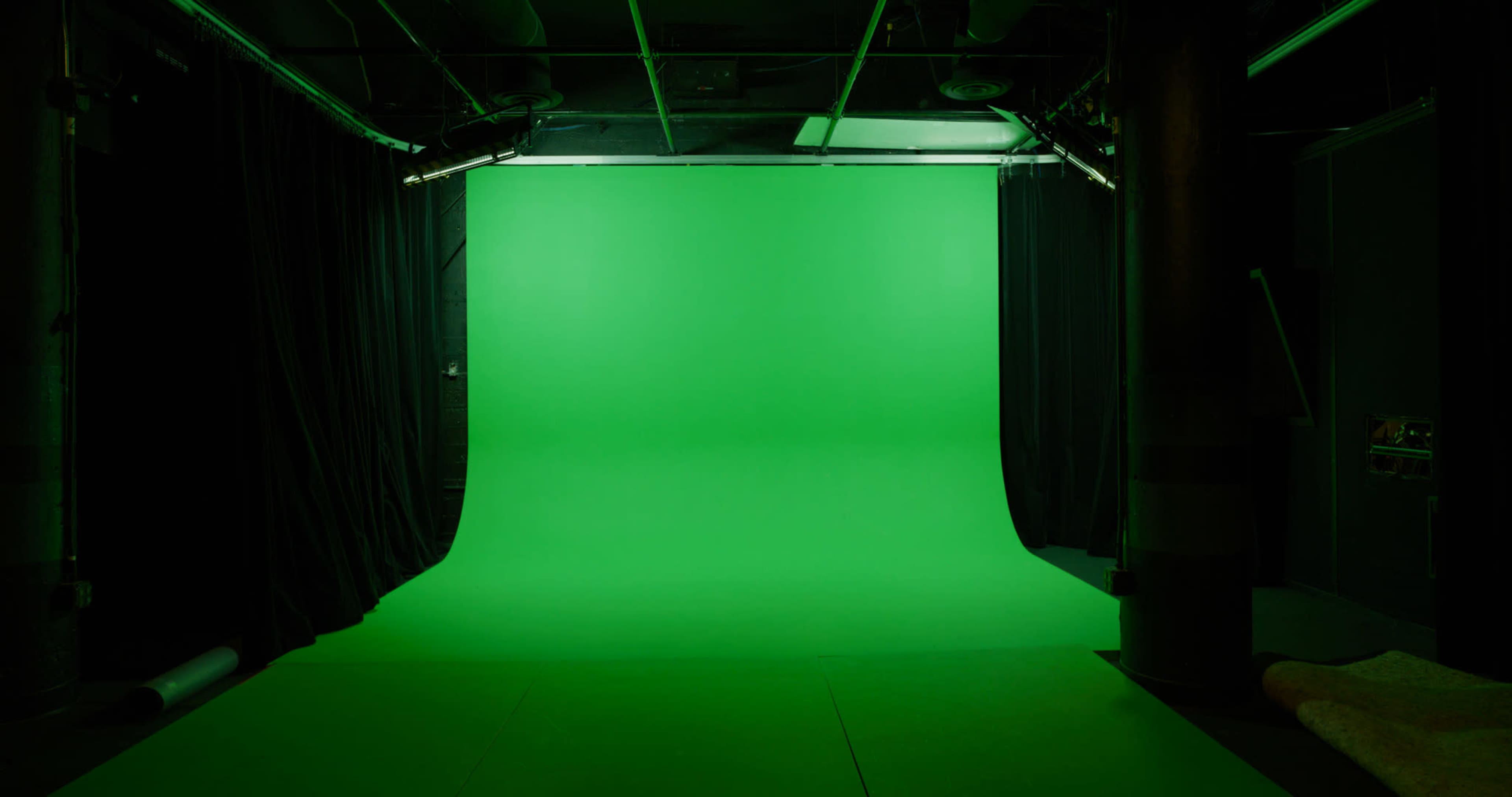 The image shows a studio space with a green backdrop, surrounded by black curtains and soft lighting.