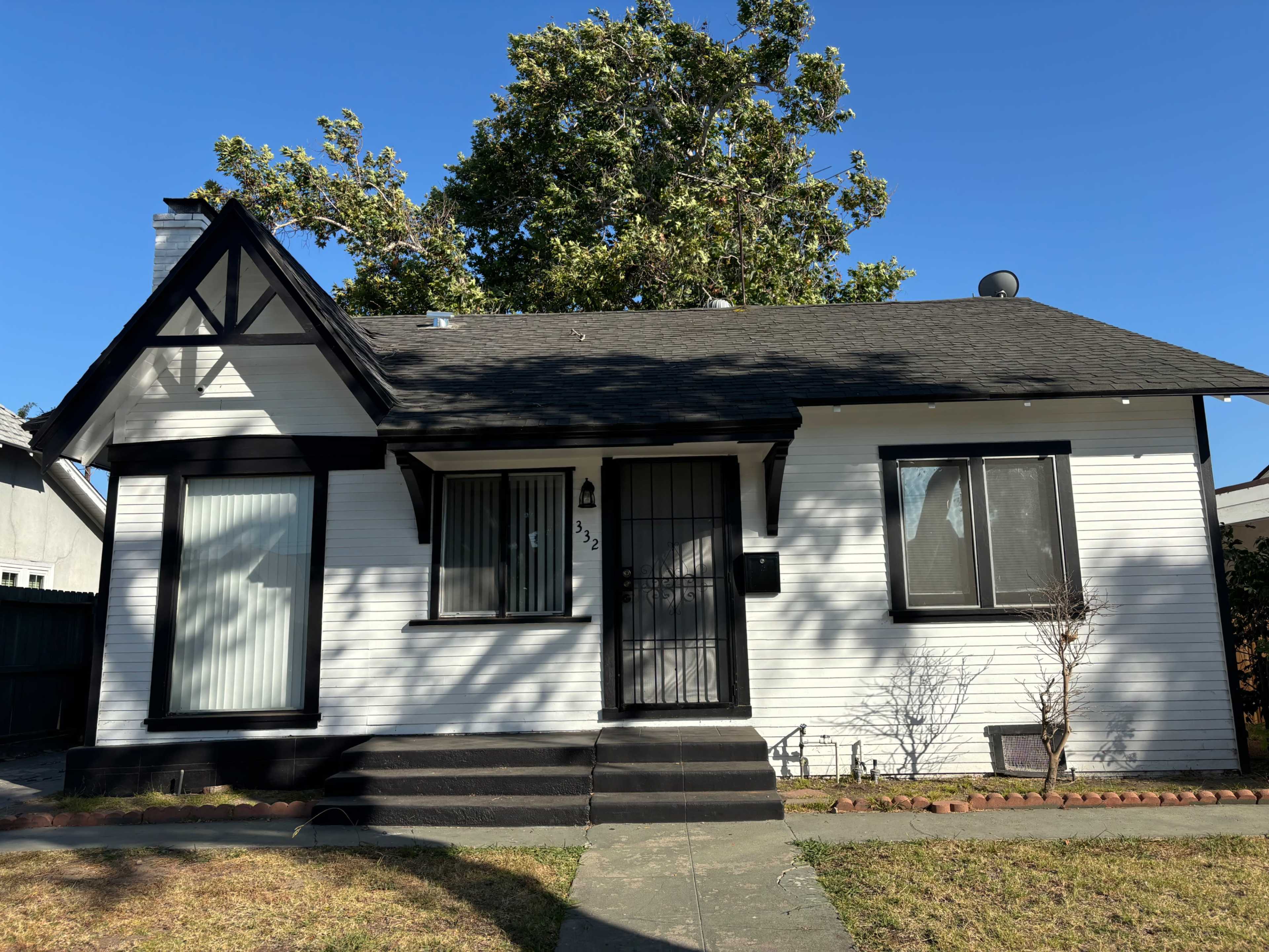 A single-story, white house with black trim features a small front porch and a lawn in the foreground.
