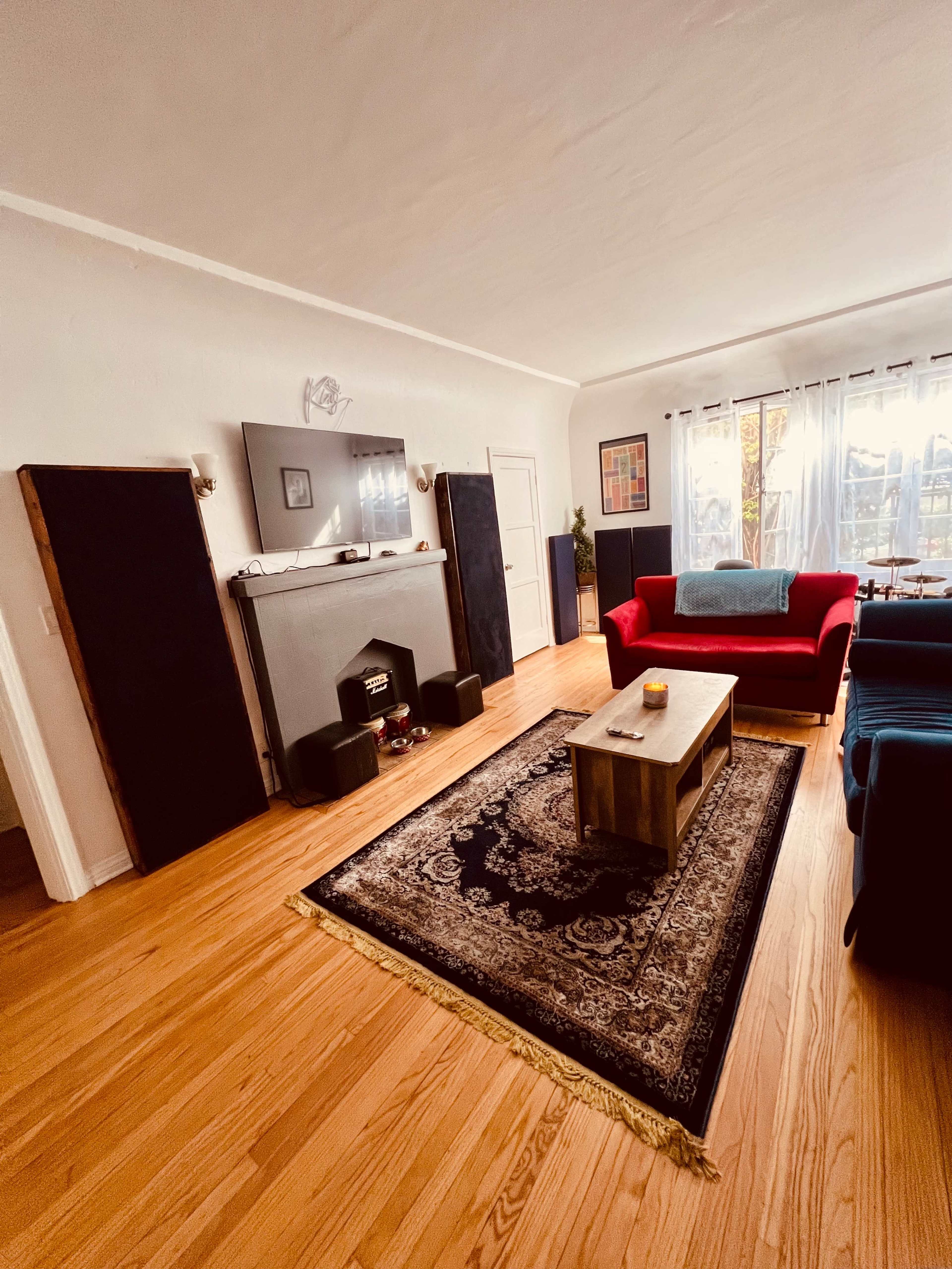 A living room with hardwood floors, a red sofa, a coffee table, a decorative rug, and a fireplace surrounded by sound equipment.