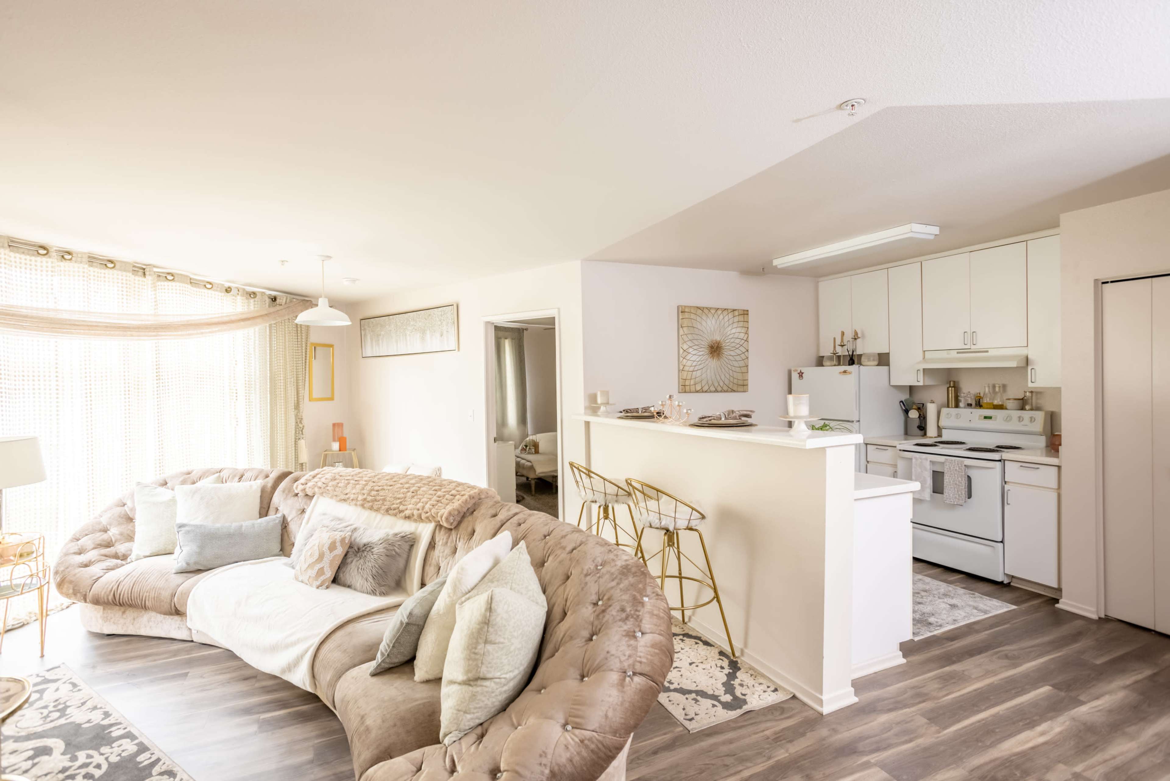 An open-concept living area and kitchen in a modern apartment, featuring a large sectional sofa and a breakfast bar with high stools.