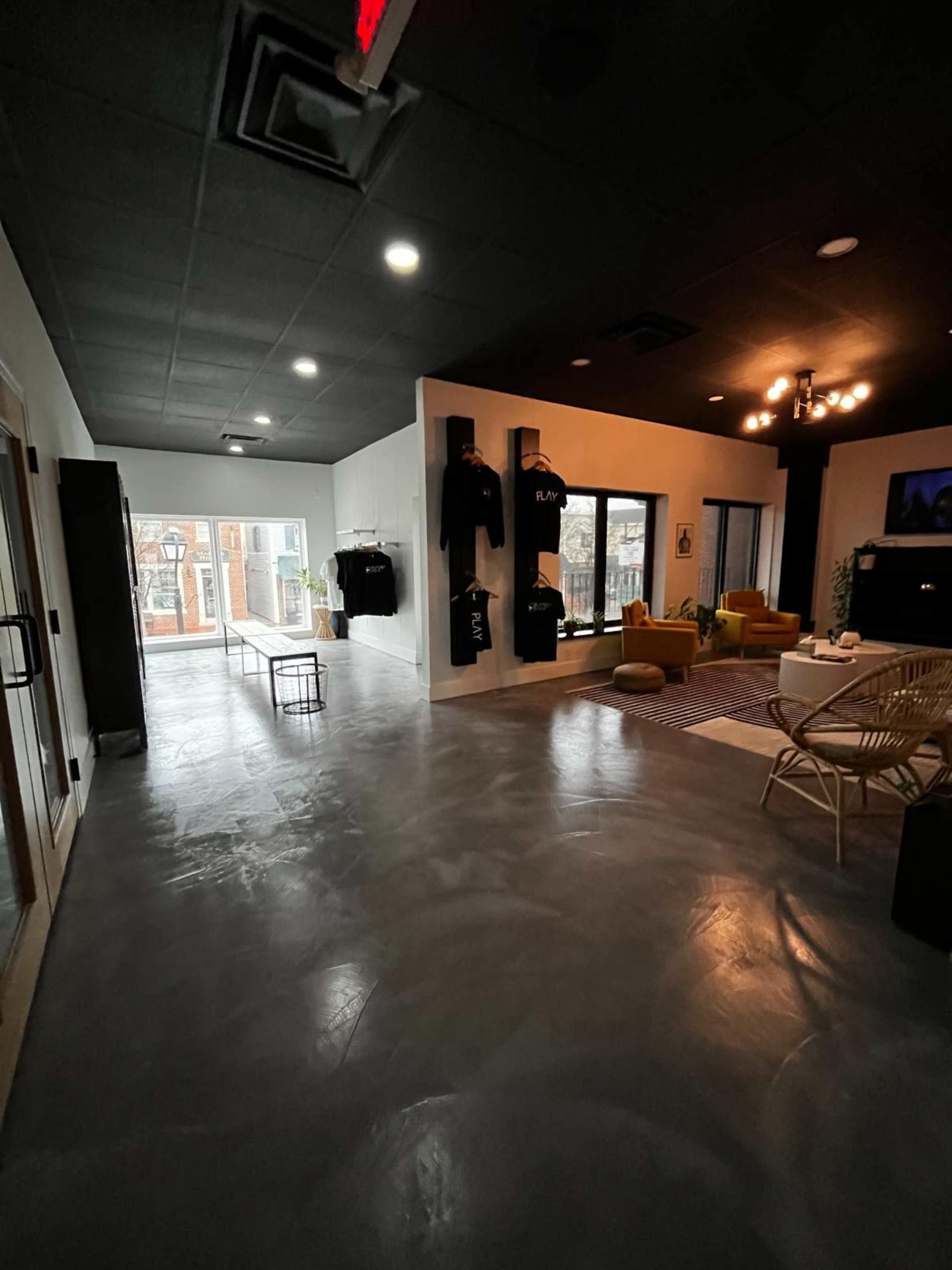 A modern interior space with a polished concrete floor, featuring a seating area, clothing racks, and large windows leading to an outdoor area.
