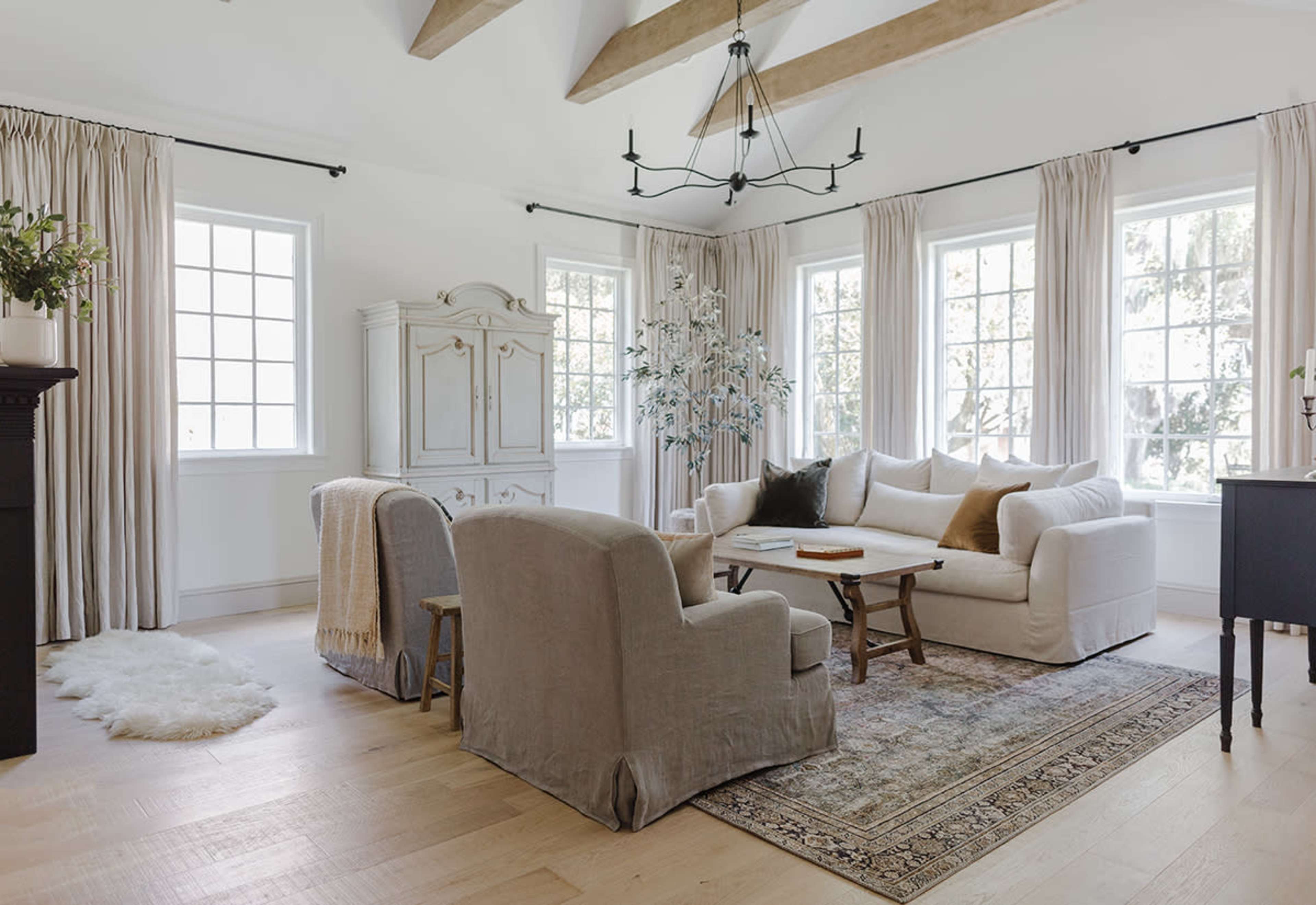 The living room features a light-colored sofa, two armchairs, a wooden coffee table, and large windows with long curtains.