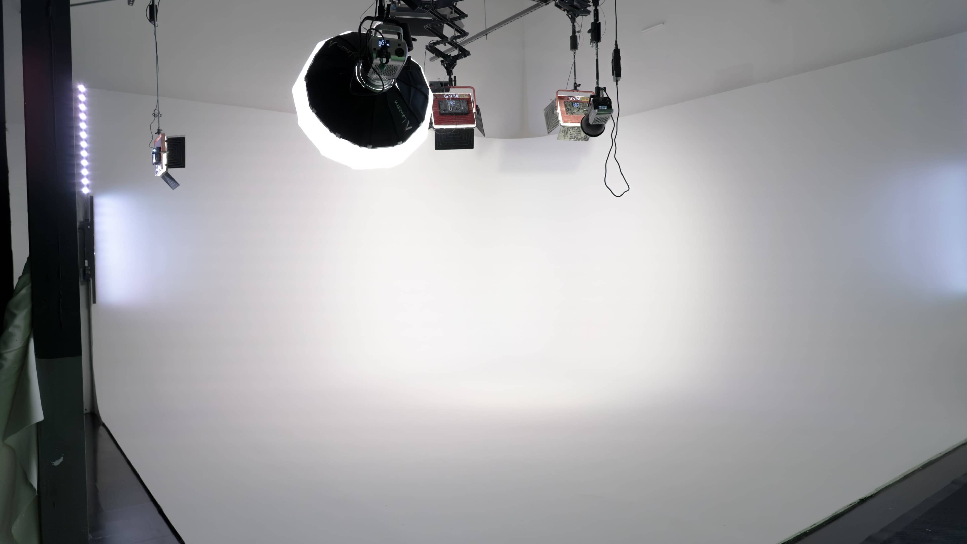 The image shows a photography studio featuring a large white backdrop and multiple lighting fixtures.