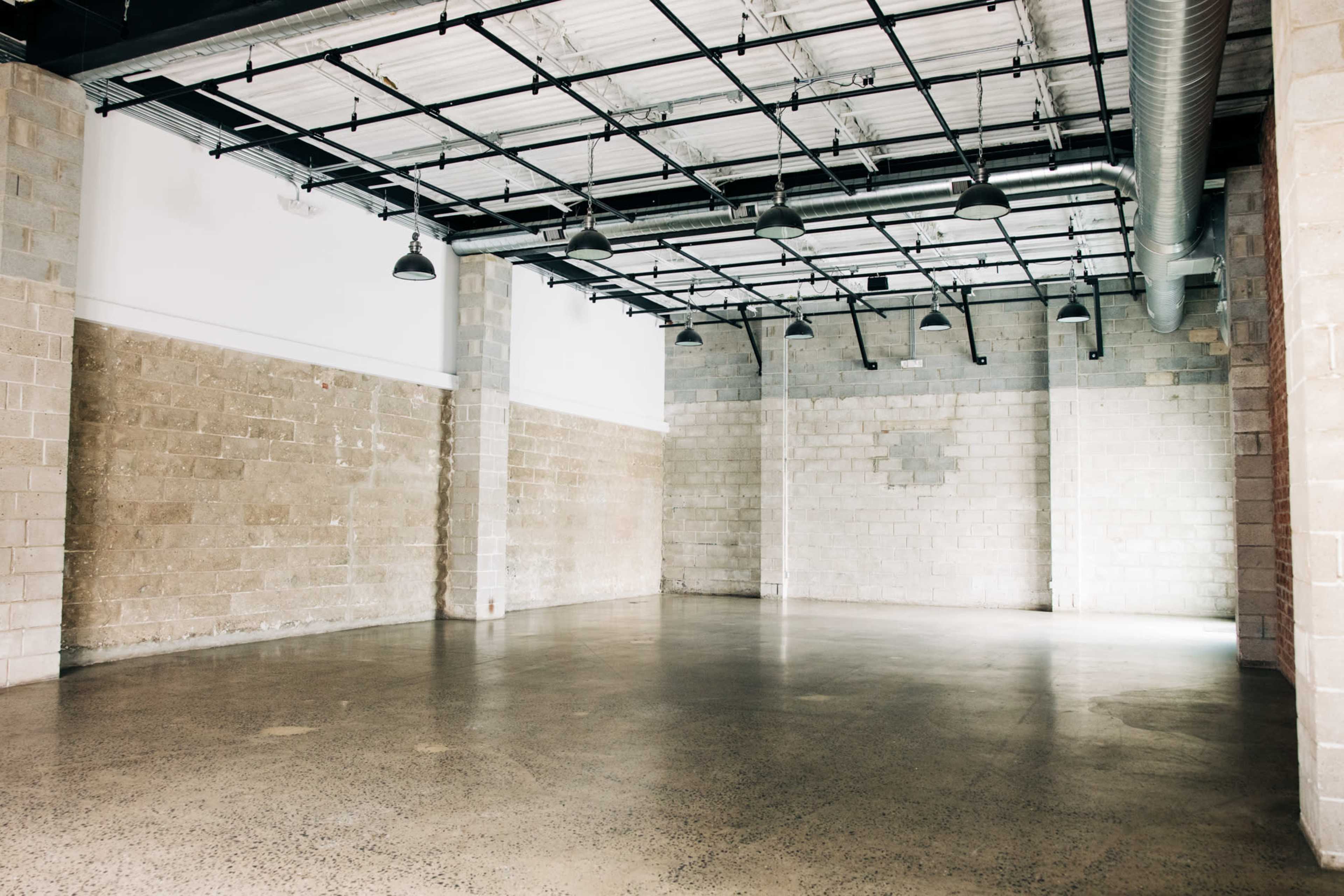 The image shows an empty industrial space with concrete walls and a polished floor, illuminated by overhead lighting.