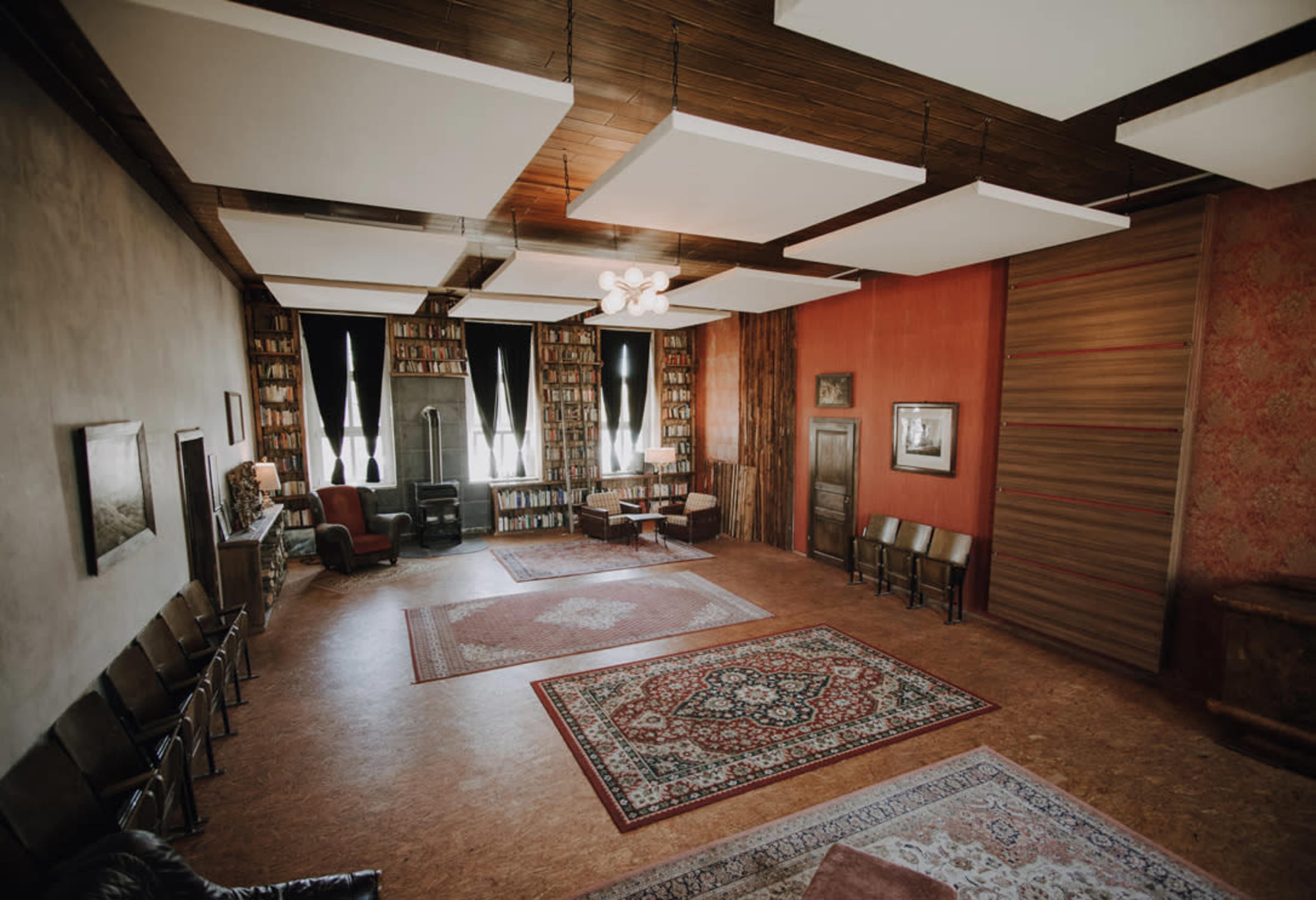 The image shows a spacious room with bookshelves lining the walls, a circular seating arrangement in the center, and decorative rugs on the floor.
