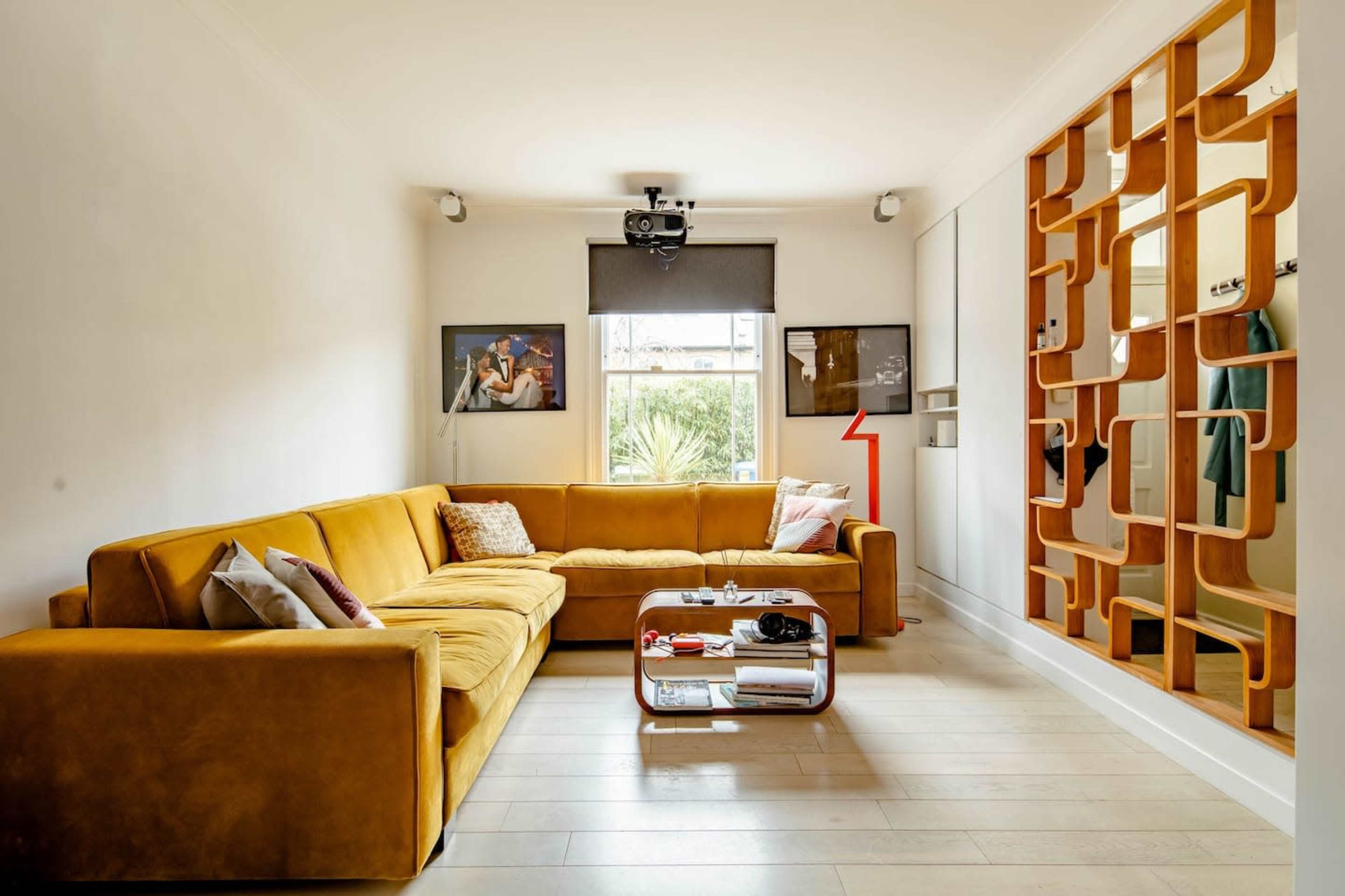 The image shows a modern living room featuring a large mustard-colored sectional sofa, a coffee table, and a wall unit with hooks and shelves.