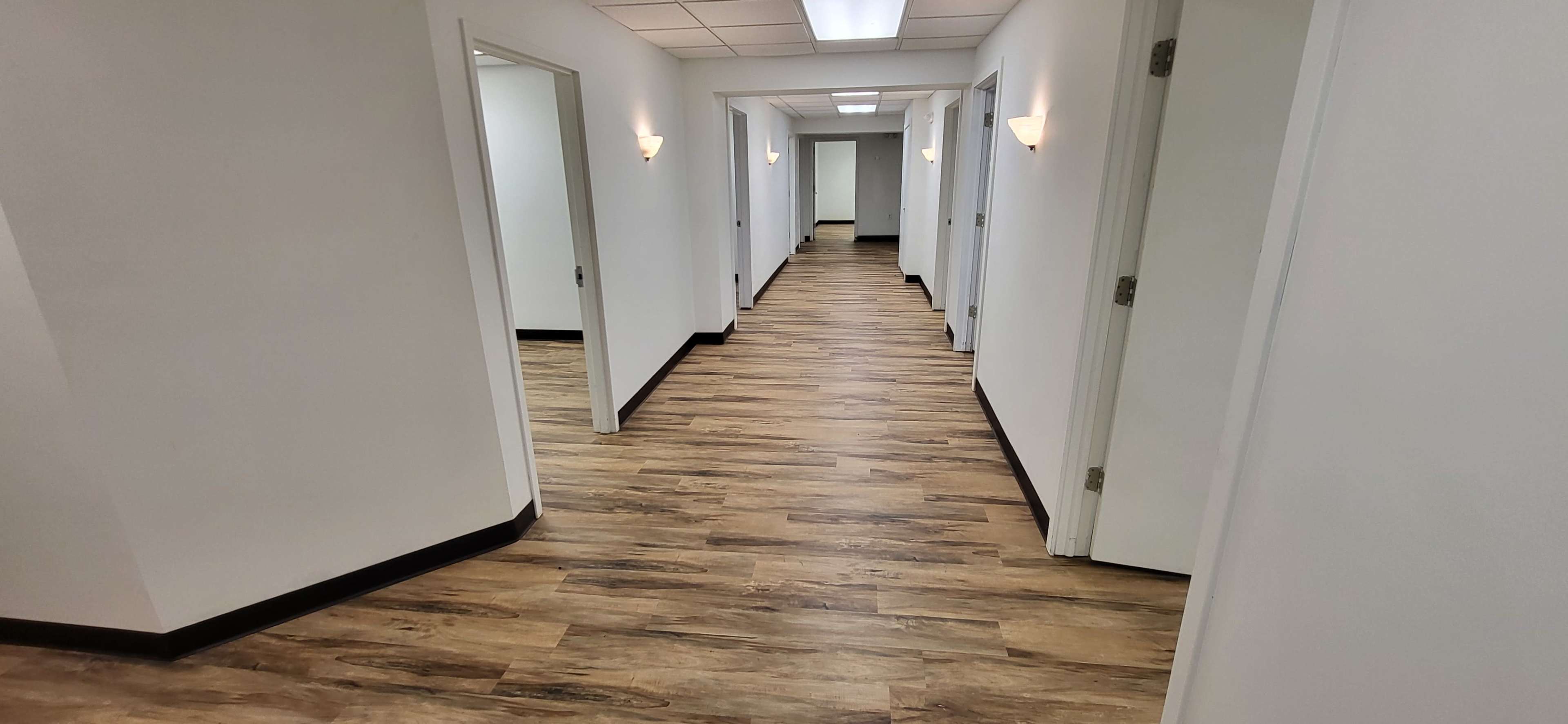 A long corridor with several doors on either side and wood-like flooring.