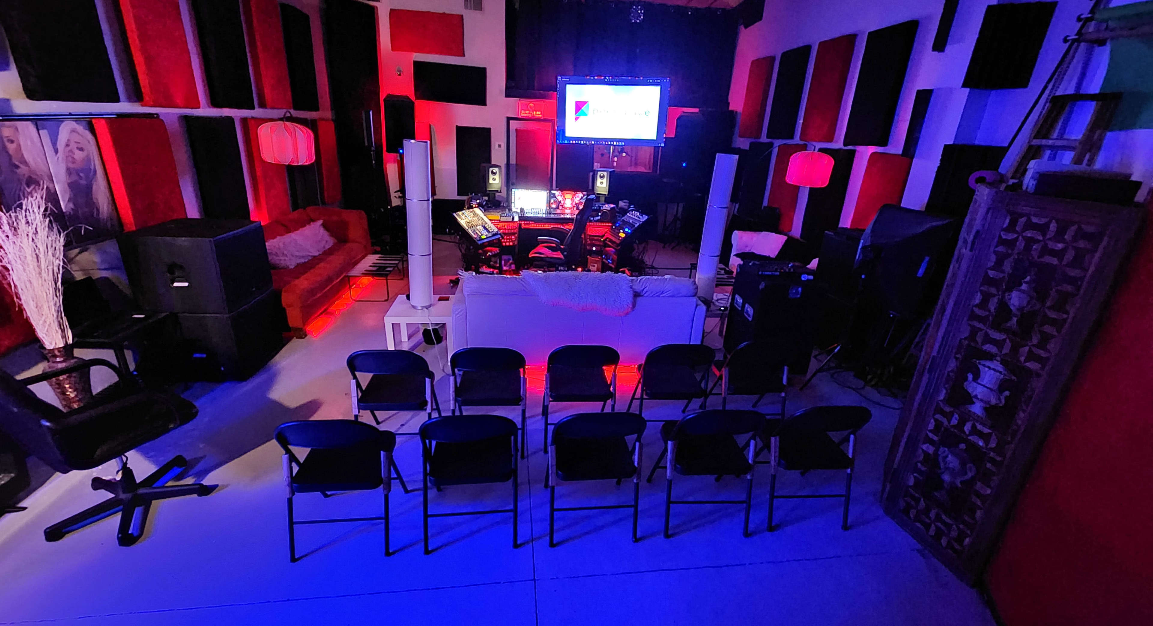 A well-equipped music studio with seating arranged facing a large screen and various audio equipment set up in a colorful environment.