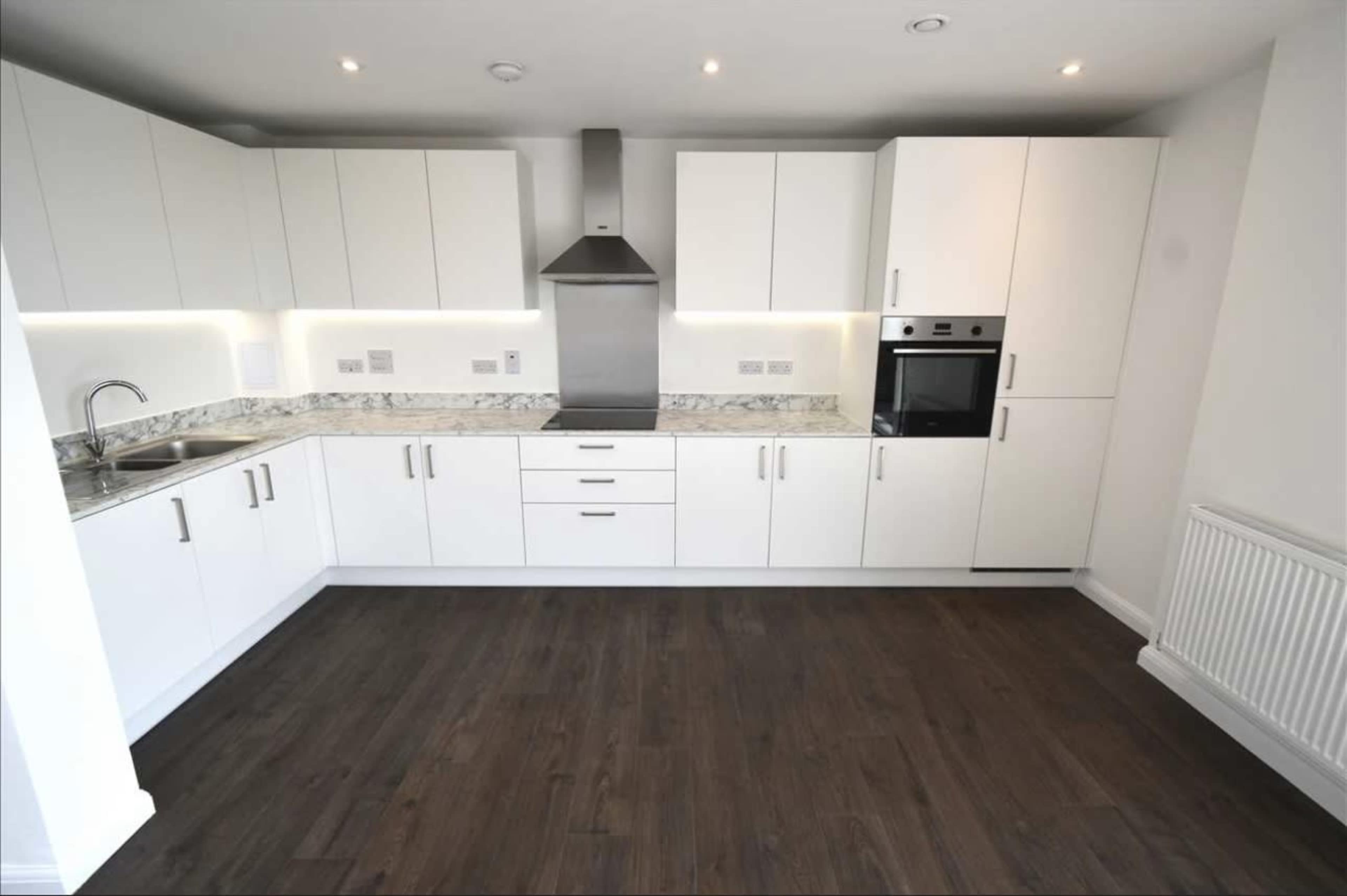 The image shows a modern kitchen with white cabinetry, a stainless steel range hood, a built-in oven, and a granite countertop.