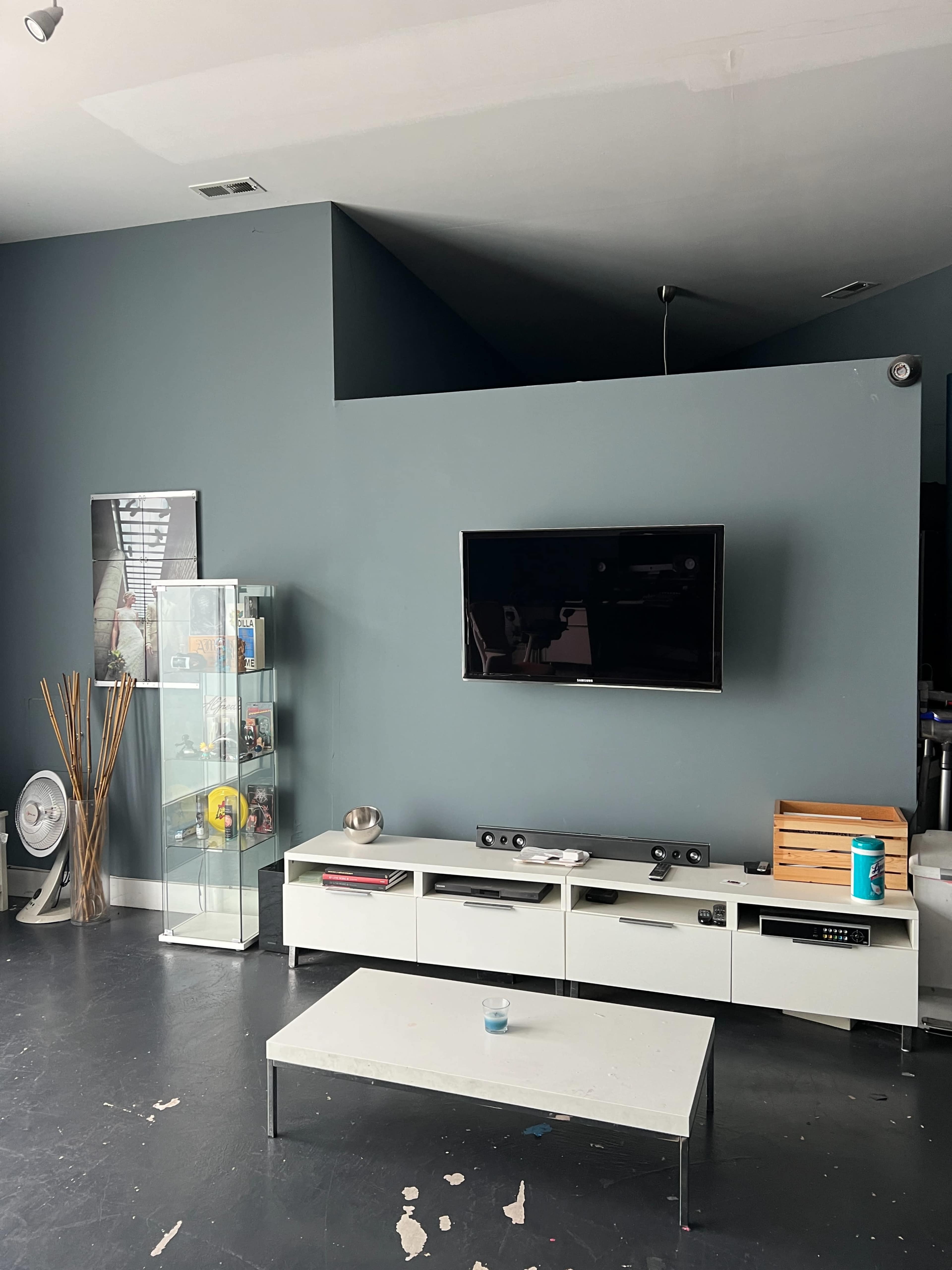 A living room with a television mounted on a gray wall, a white coffee table, a minimalist TV stand, and a glass display case.