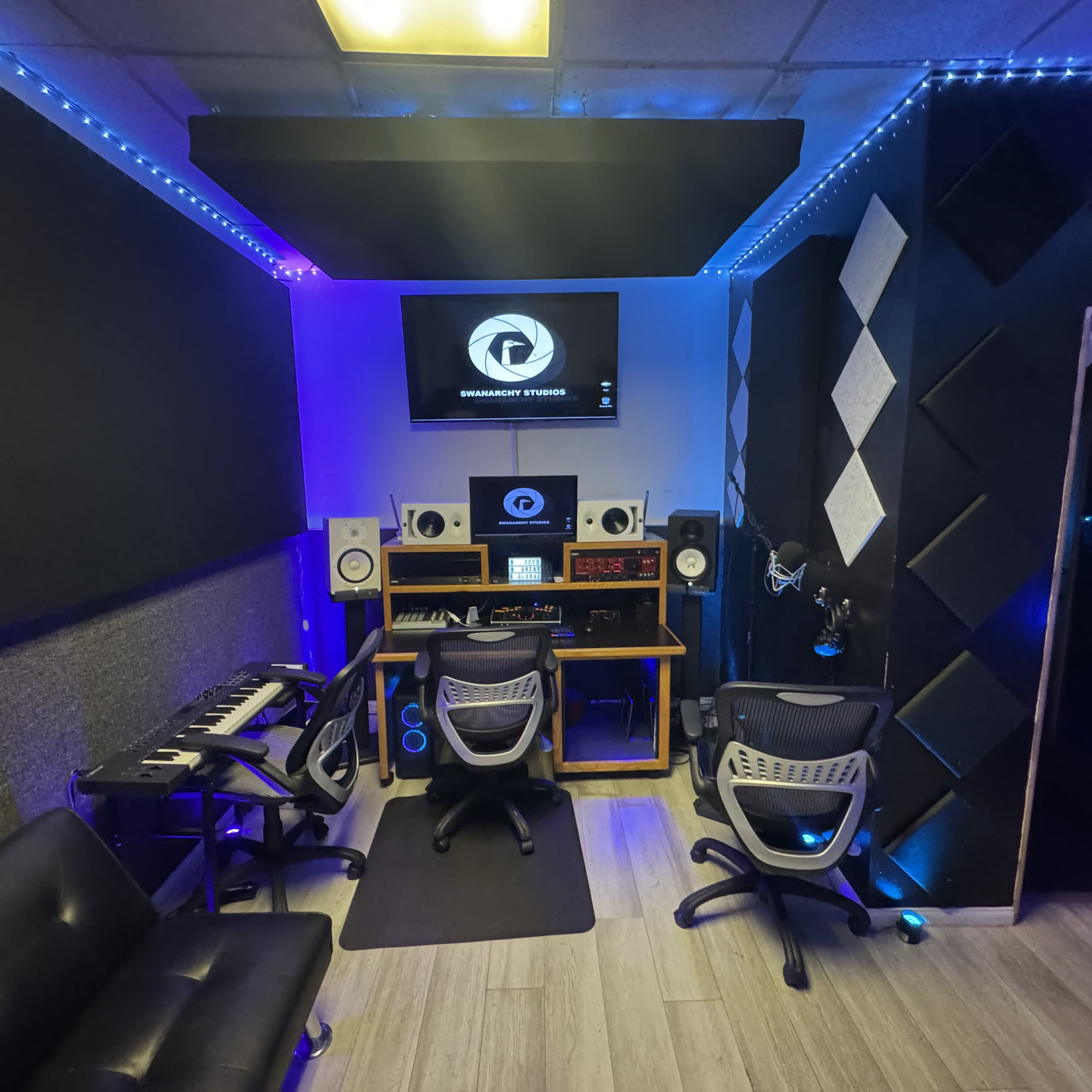 The image shows a modern music studio with soundproofing panels, a computer workstation, and various audio equipment, illuminated by blue and white LED lights.