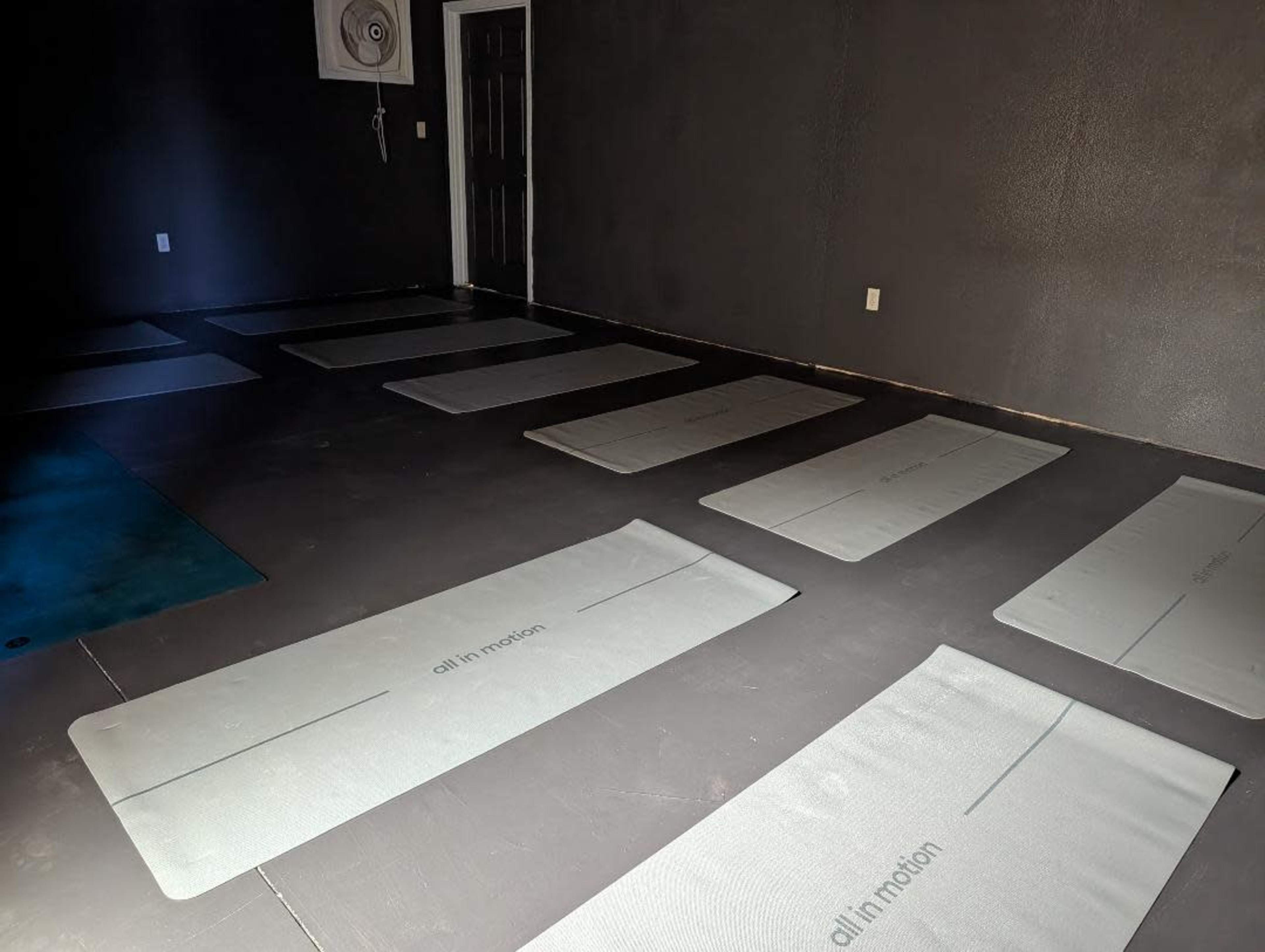 The image shows an empty room with several exercise mats arranged on the floor against a dark wall.
