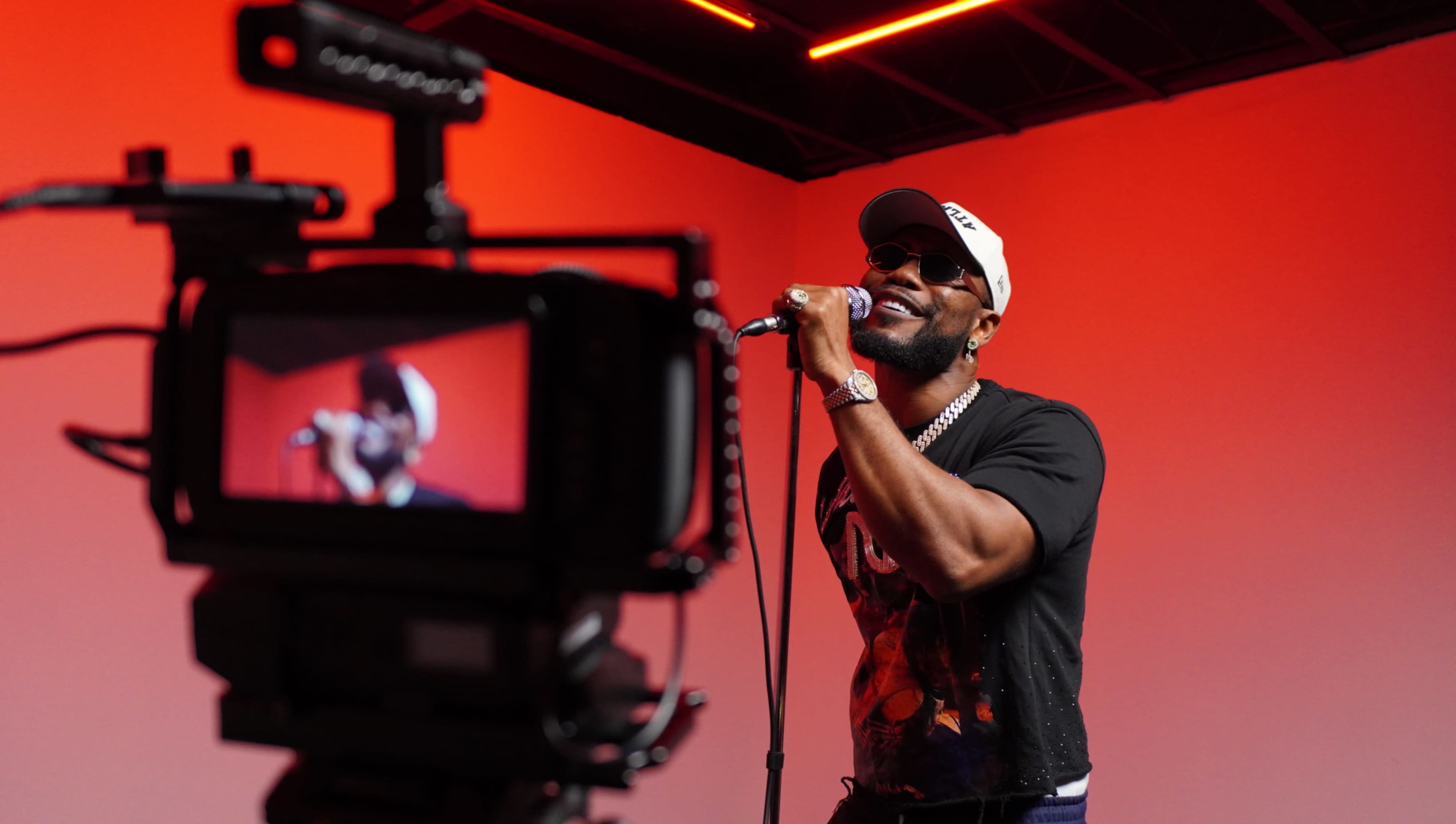 A singer performs on stage while being filmed against a backdrop of red lighting.