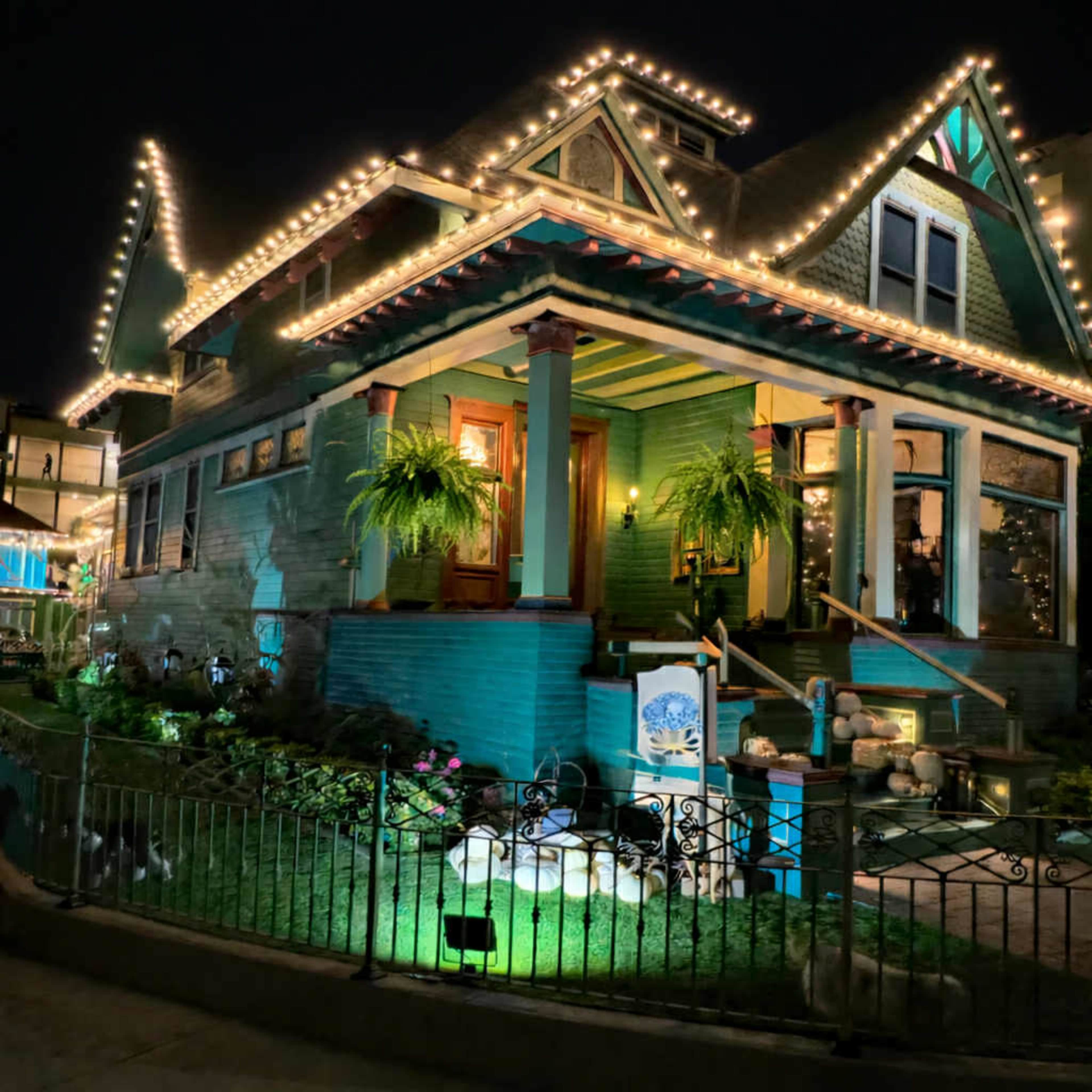A two-story house with a colorful facade is adorned with string lights and has a well-maintained garden in front.