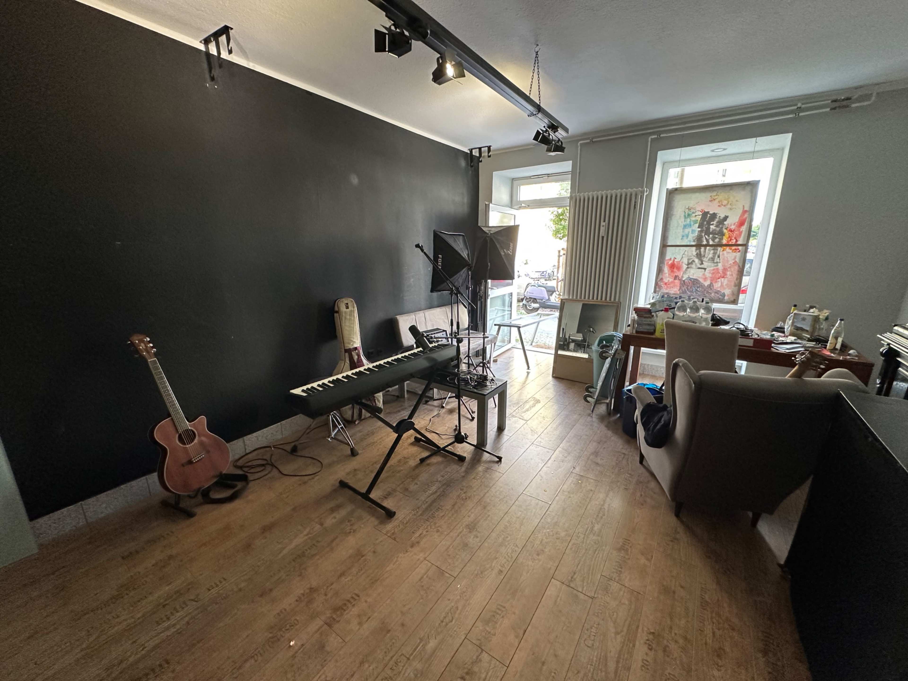 A room features a black wall, a guitar, a keyboard on a stand, and a mix of furniture, including a table and chairs, with items scattered around.
