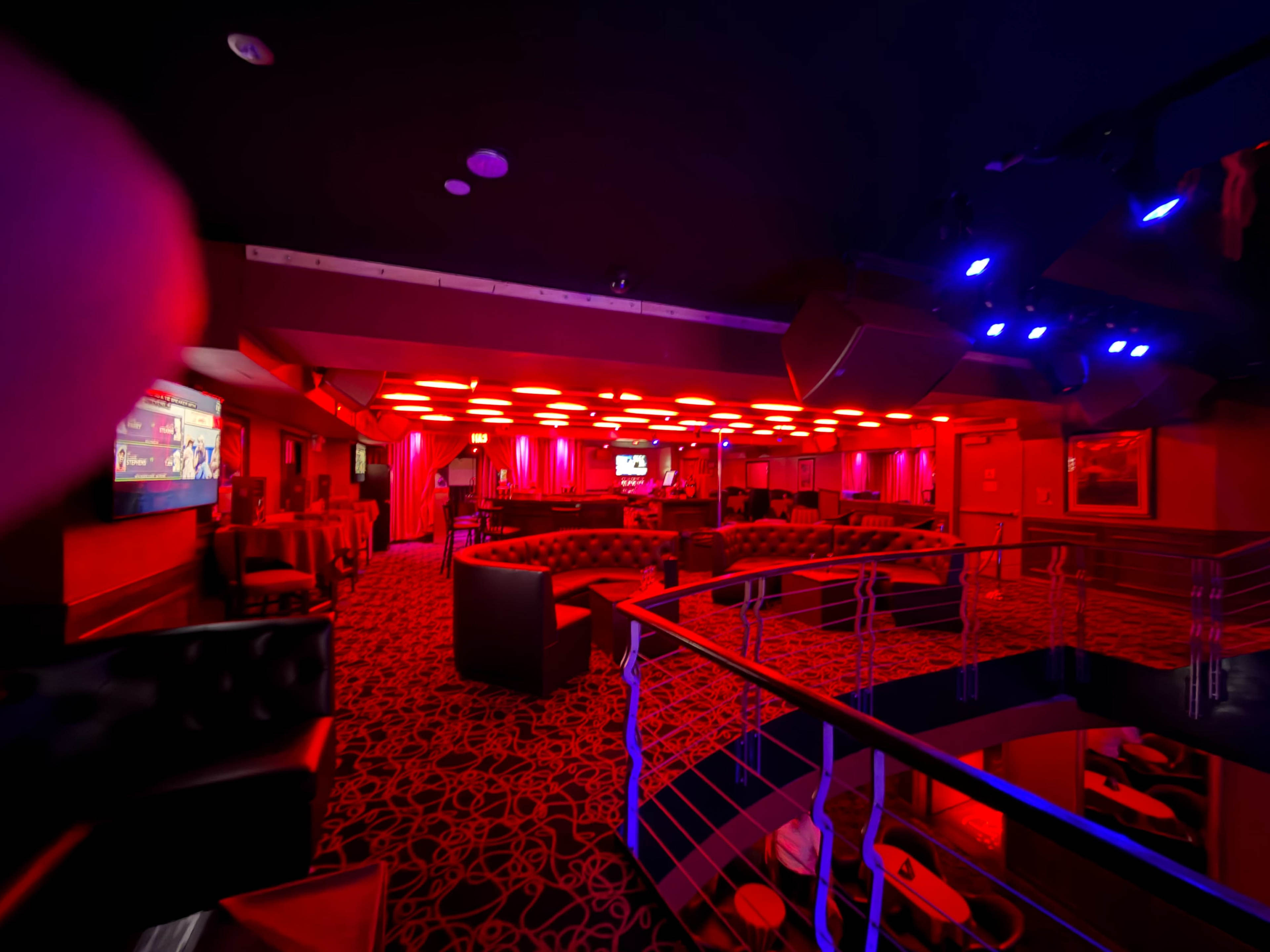 The image shows the interior of a dimly lit lounge featuring red lighting, seating areas with dark upholstery, and a modern design.