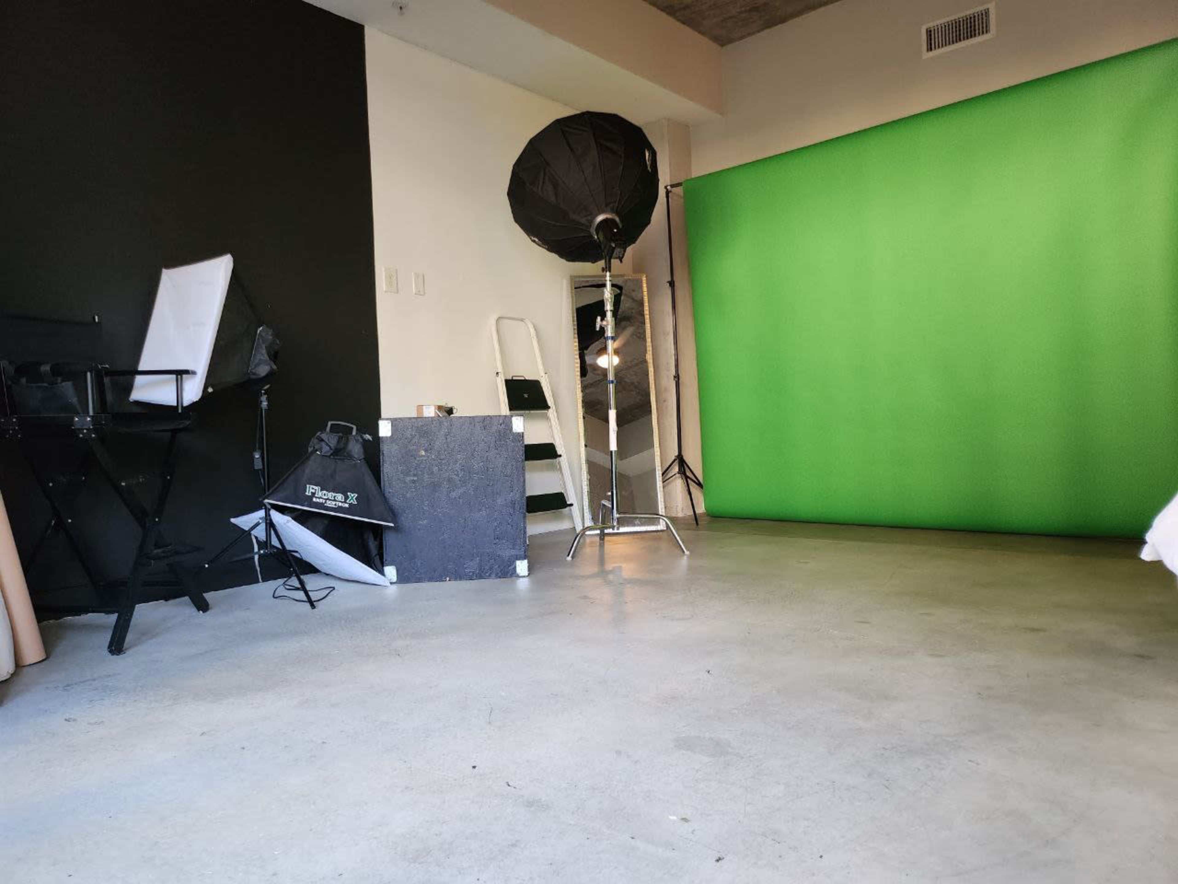 The image shows a photography studio with a green backdrop, a lighting setup, and various props arranged on the floor.