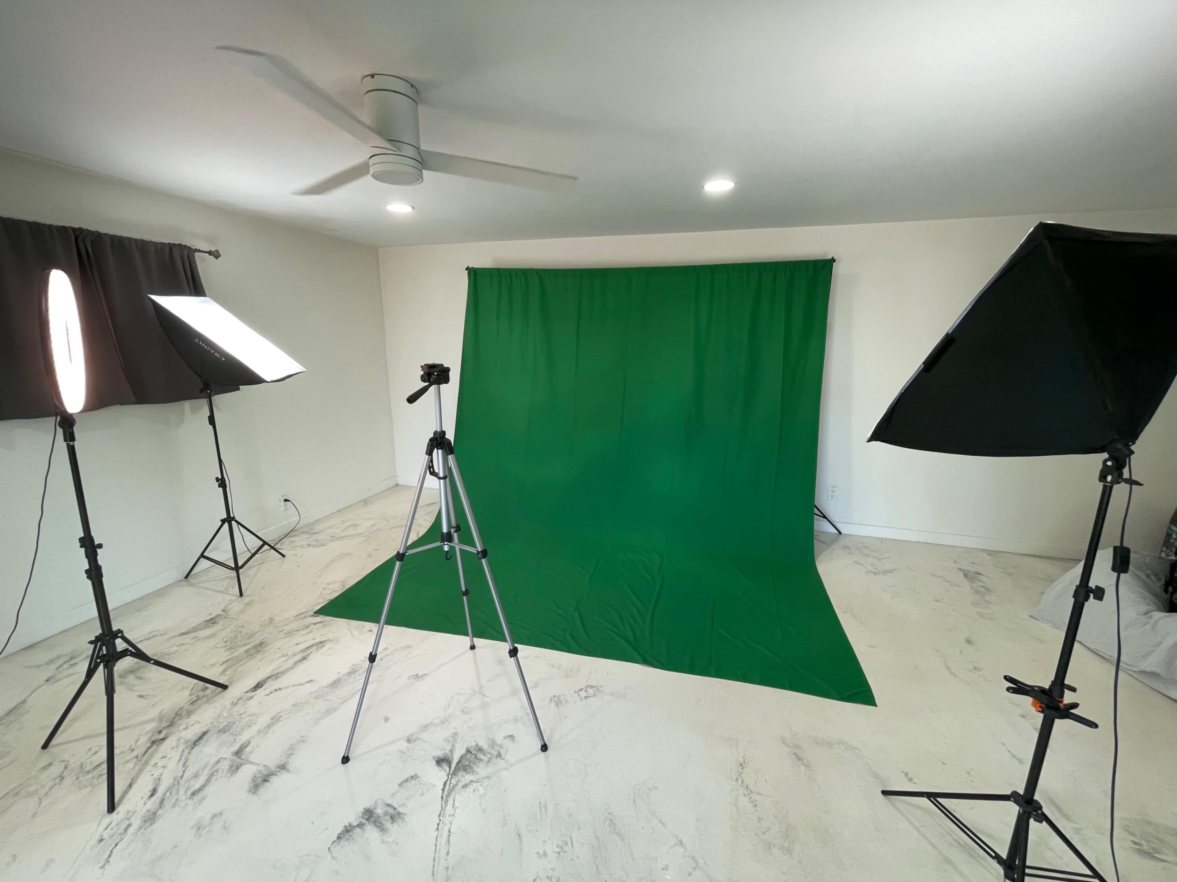 A photo studio setup with a green backdrop, lighting equipment, and a camera on a tripod.