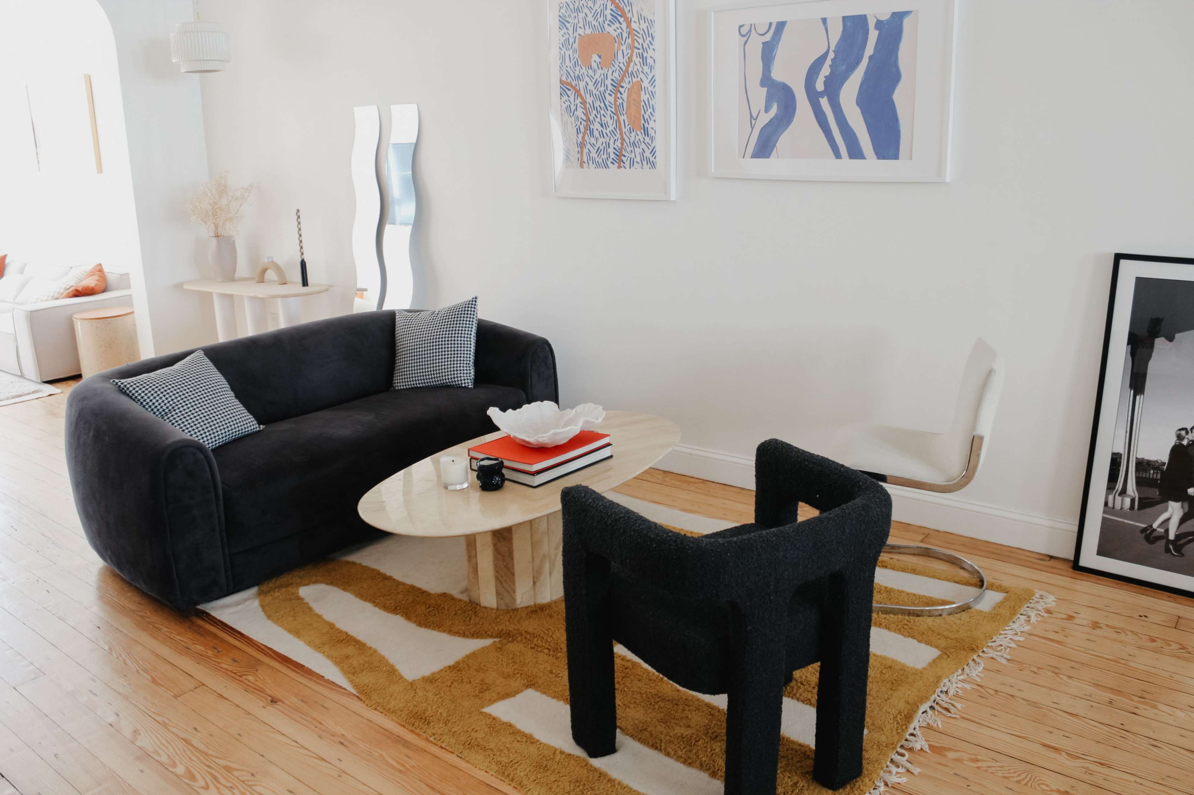 A modern living room features a dark sofa, a round marble coffee table, and a textured chair, all arranged on a patterned area rug.