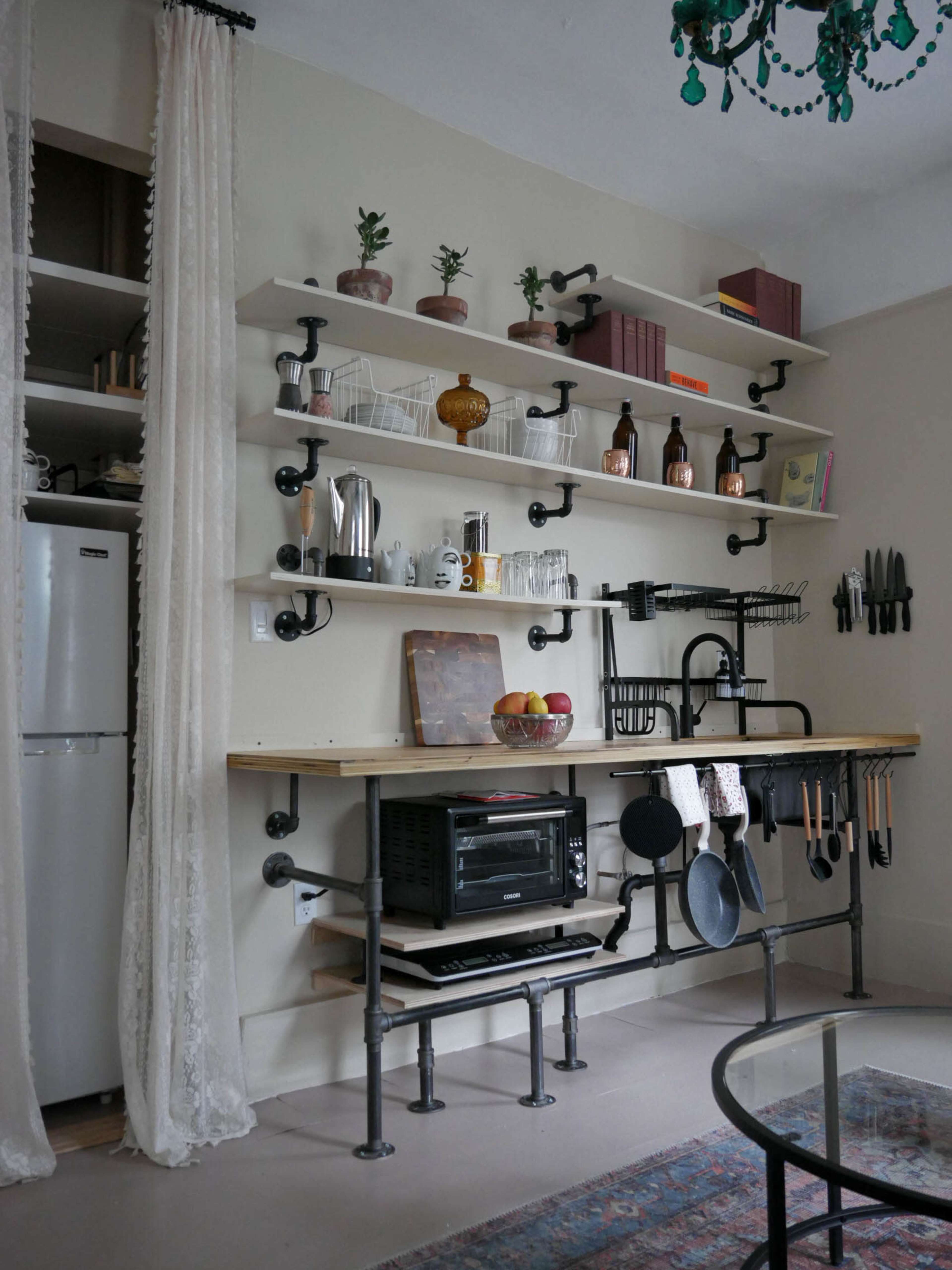 A minimalist kitchen with industrial-style shelving, featuring a wooden countertop, a variety of kitchen utensils, and decorative plants.
