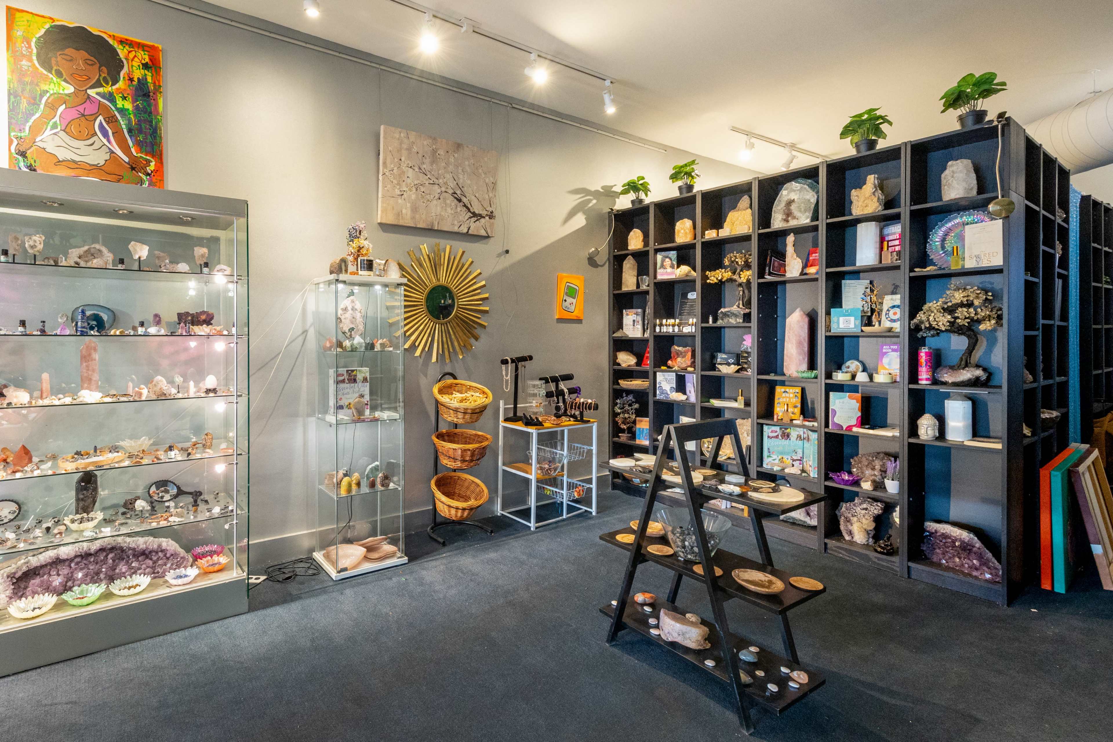 A well-organized store interior displaying various crystals, decorative items, and artwork on the walls, with a showcase and shelves filled with merchandise.