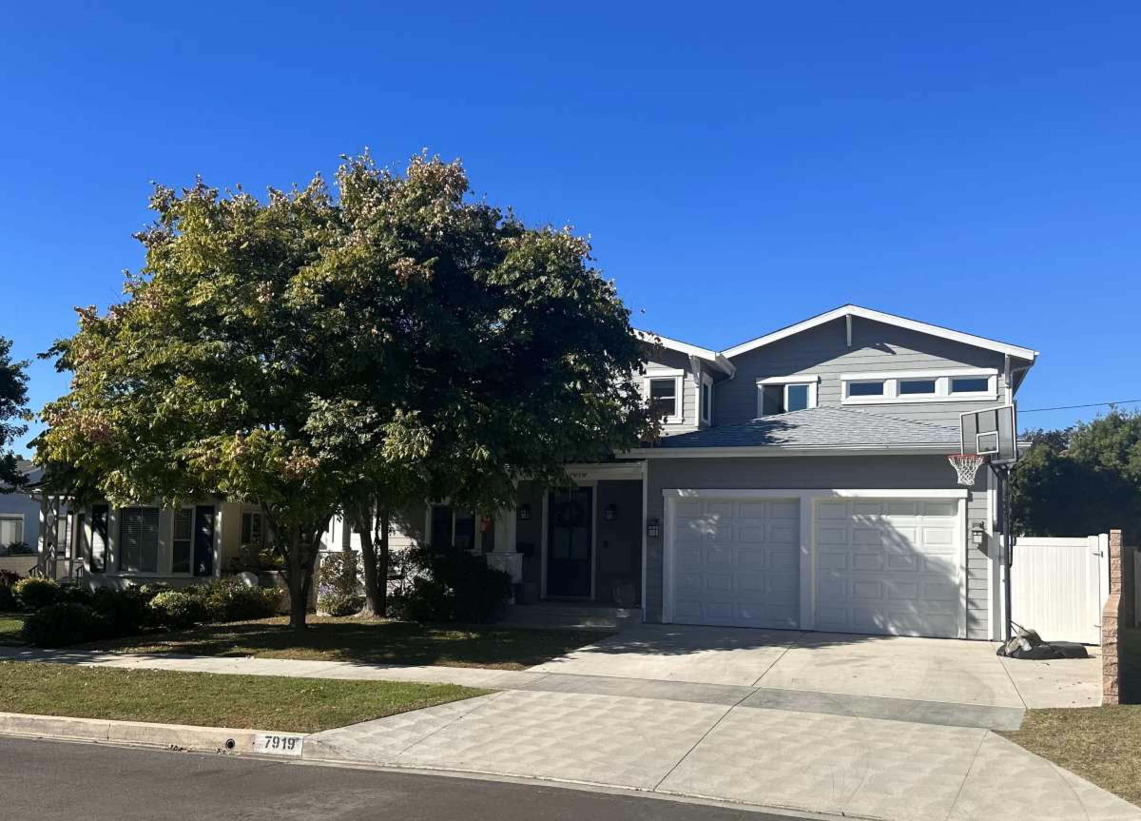 The image shows a two-story house with a basketball hoop attached to the garage, surrounded by trees and a well-maintained lawn.