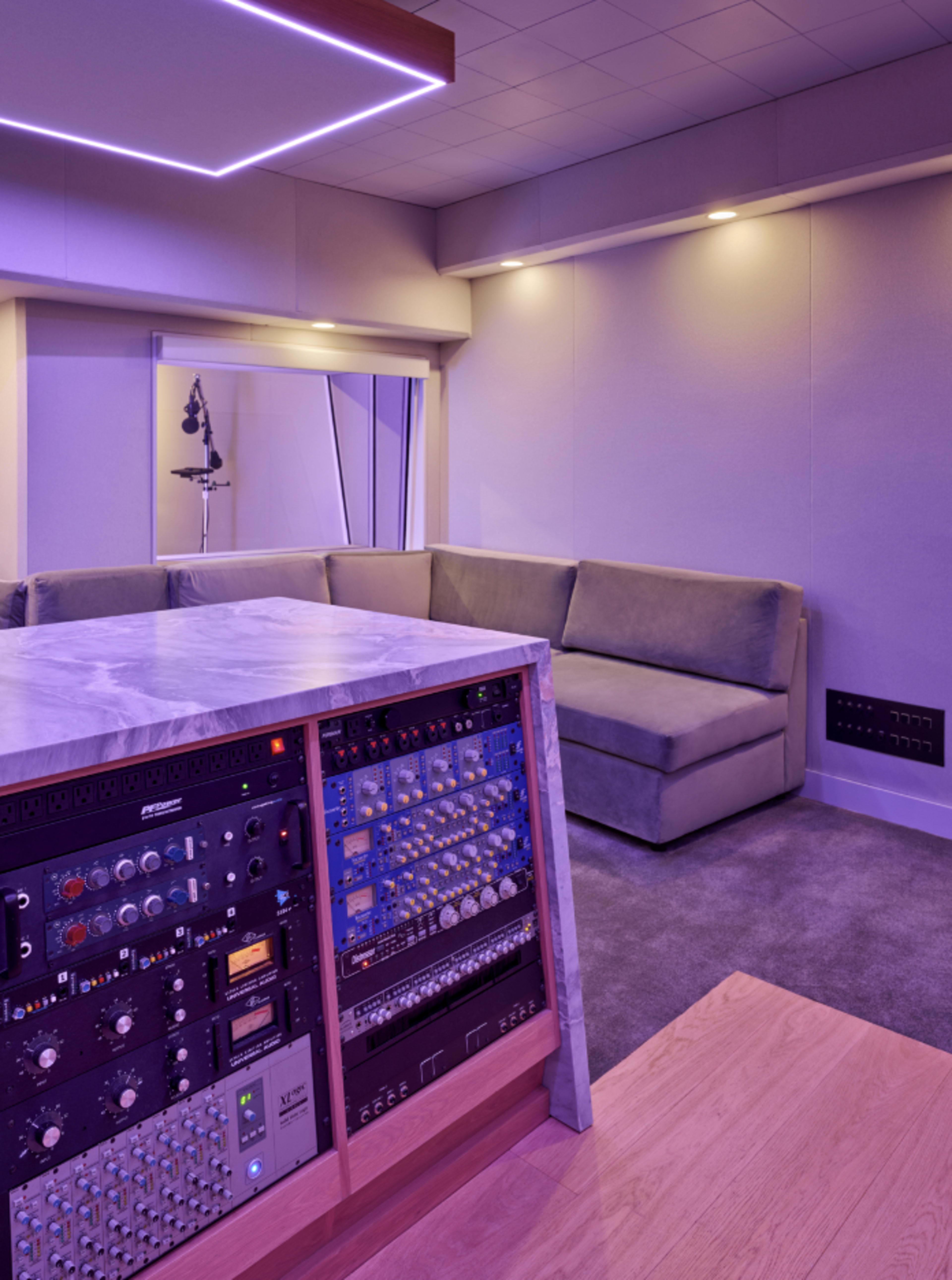 The image shows a modern sound recording studio with a marble counter, various sound equipment, and a gray sectional couch under purple lighting.
