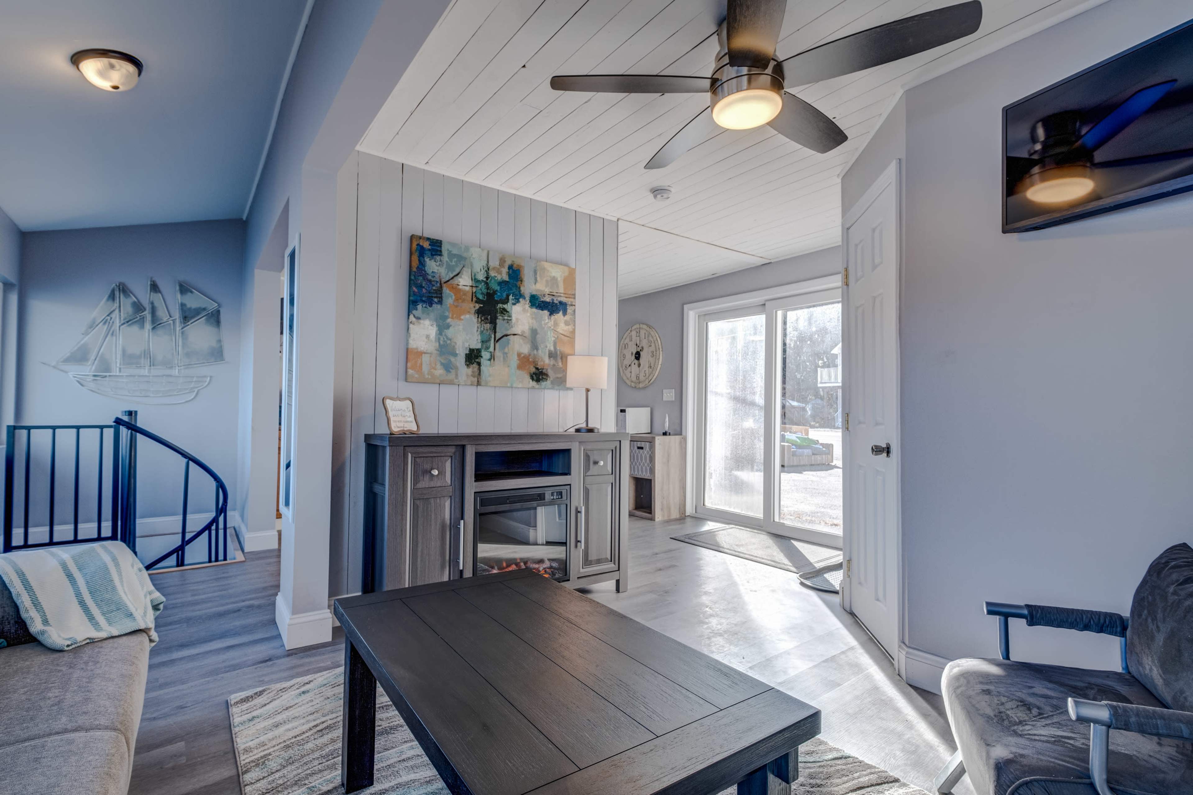 A modern living room features a gray sofa, a dark wood coffee table, and a view of a patio through sliding glass doors.