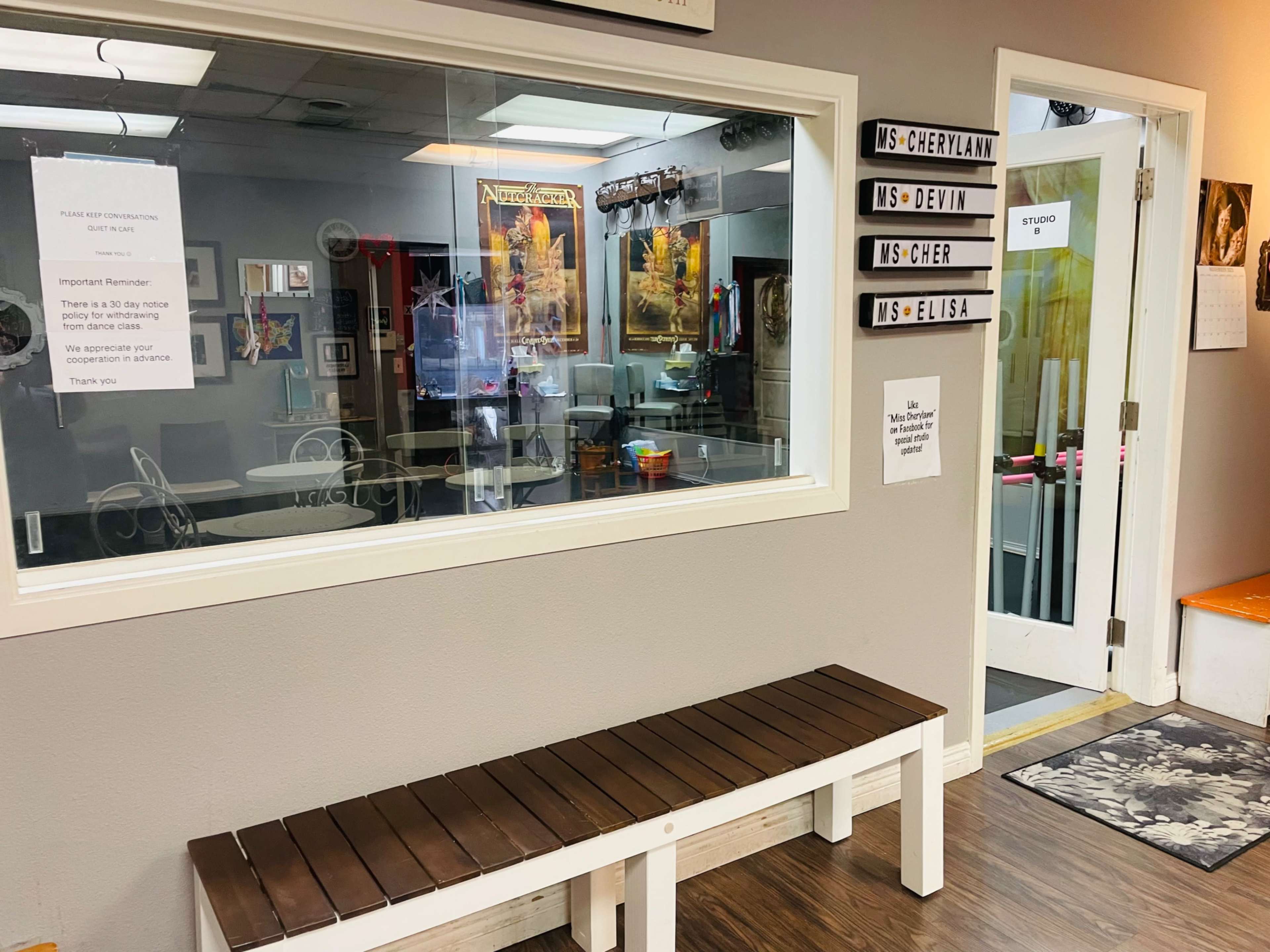 The image shows a waiting area with a wooden bench outside a glass-enclosed studio that features various posters and signs.