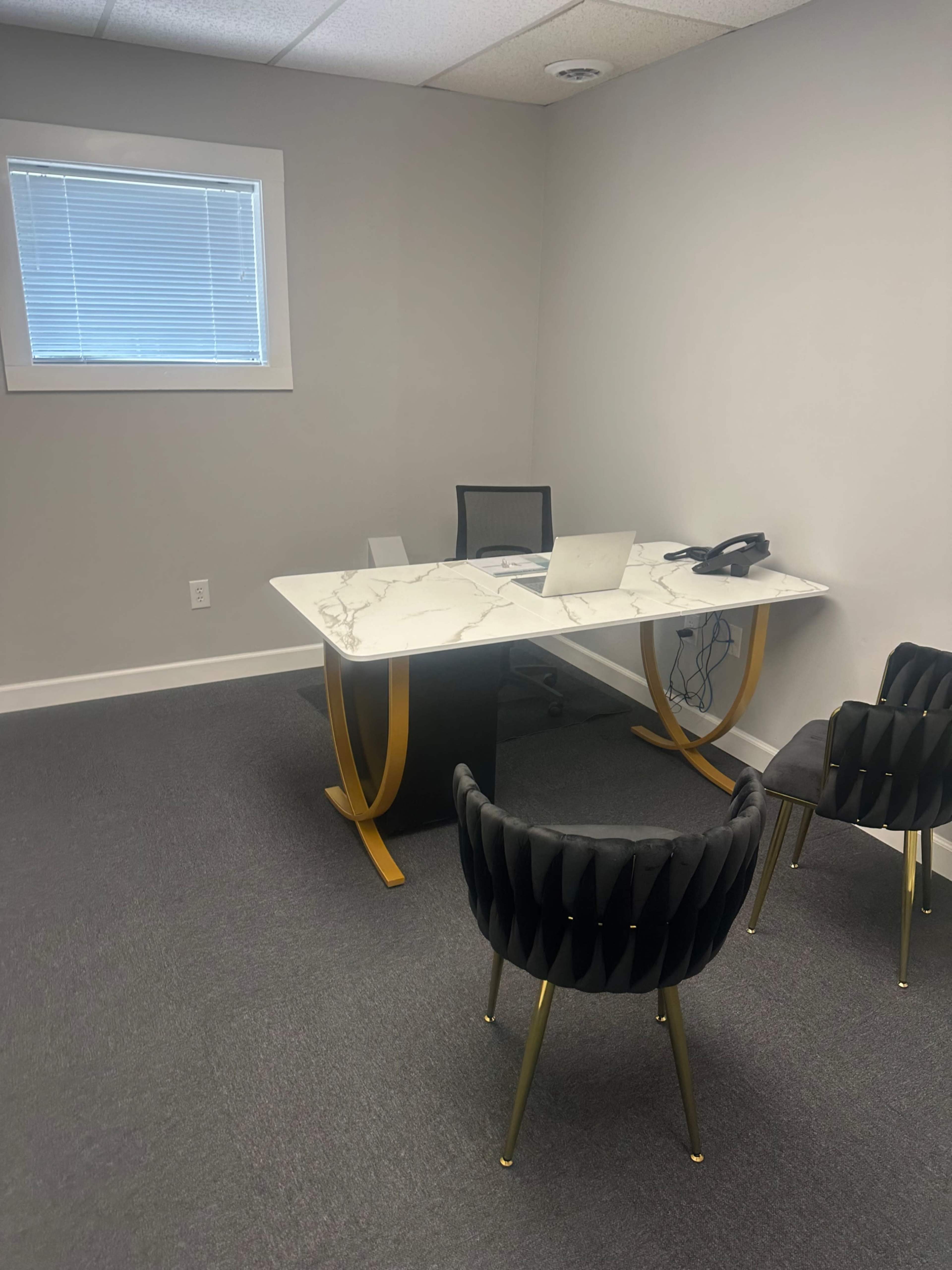 The image shows a modern office space featuring a marble-topped desk with a chair, a computer, and a phone, accompanied by two black velvet chairs with gold legs.