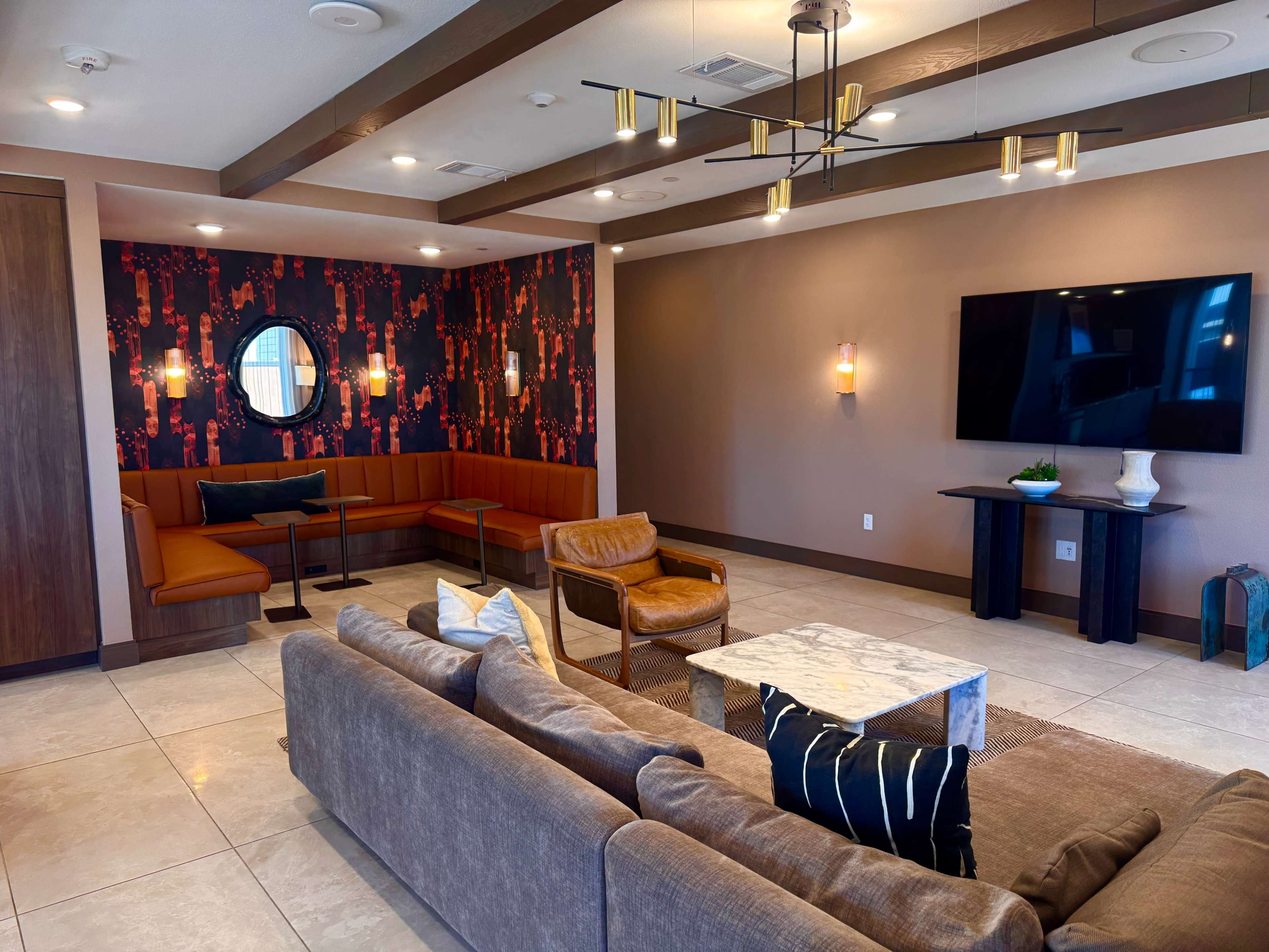 The image shows a modern lounge area featuring a sofa, armchair, decorative wall, and a television mounted on the wall.