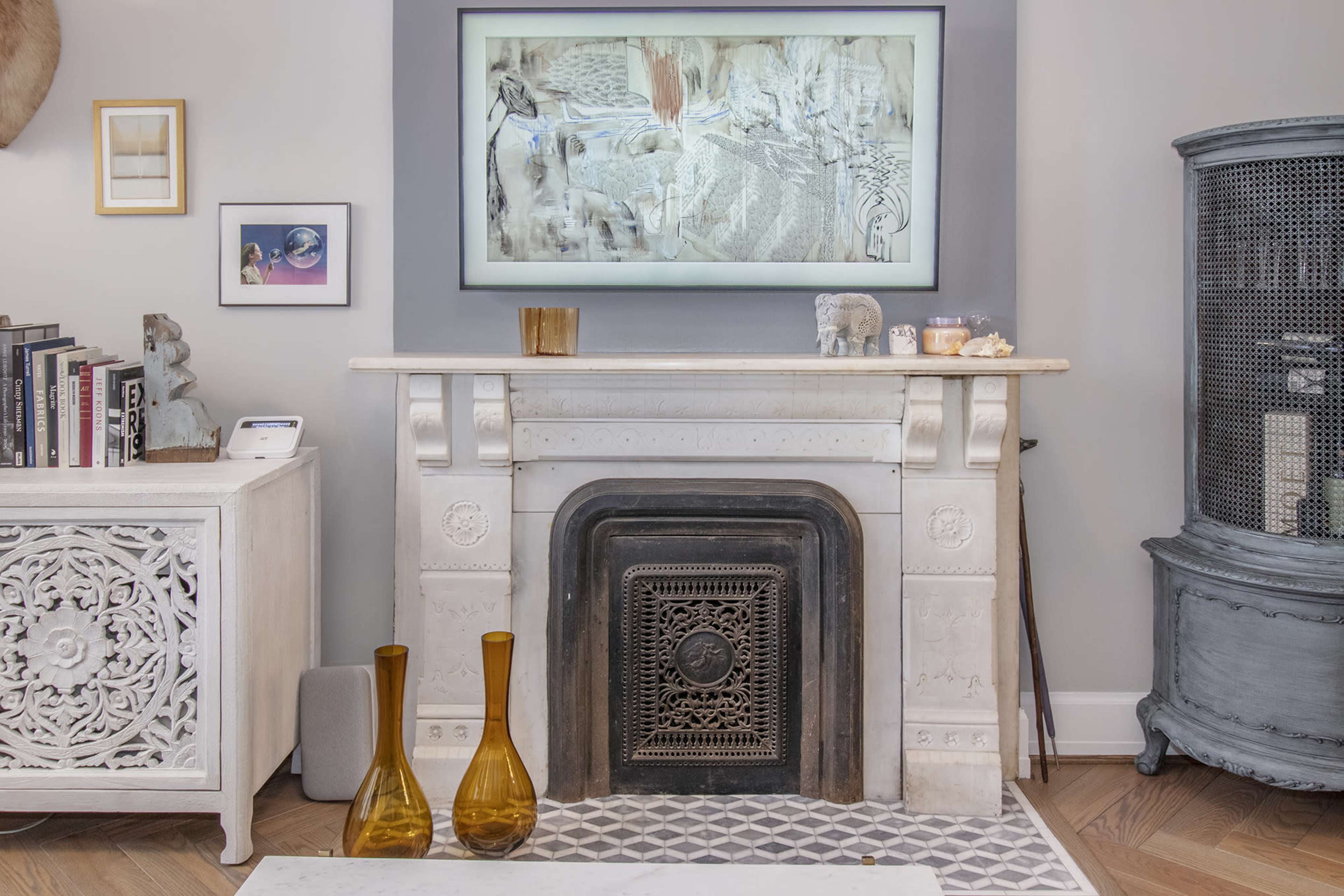 A decorated living room featuring a white mantel with a decorative fireplace, accompanied by a large piece of artwork above it and stylish decor items on both sides.