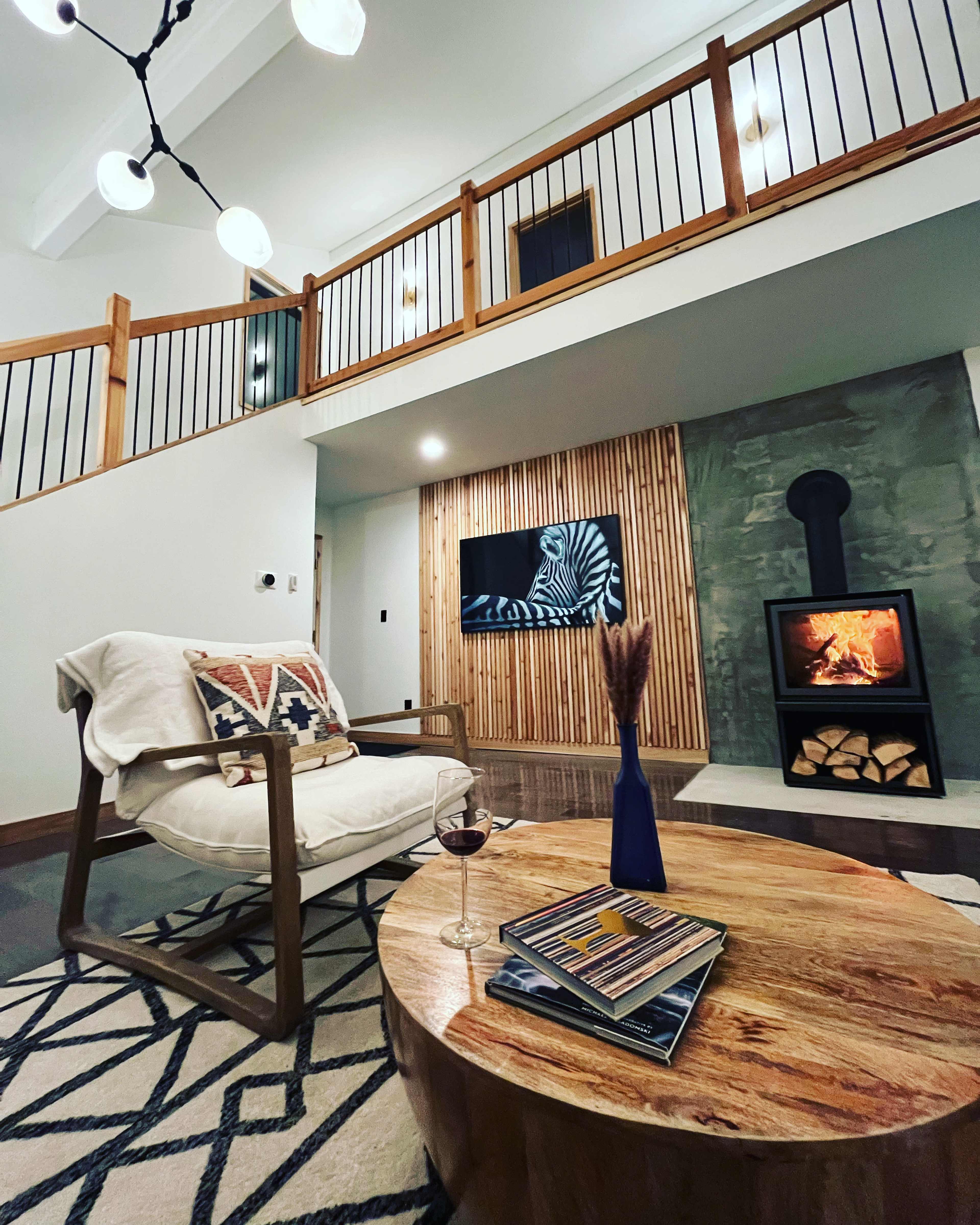 The living room features a modern design with a fireplace, a large wooden coffee table, and a chair, complemented by decorative elements and a television mounted on the wall.